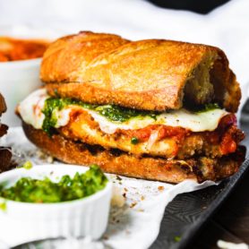 a photo of a chicken parm sandwich made on garlic bread with juicy chicken, melted mozzarella cheese and pesto.