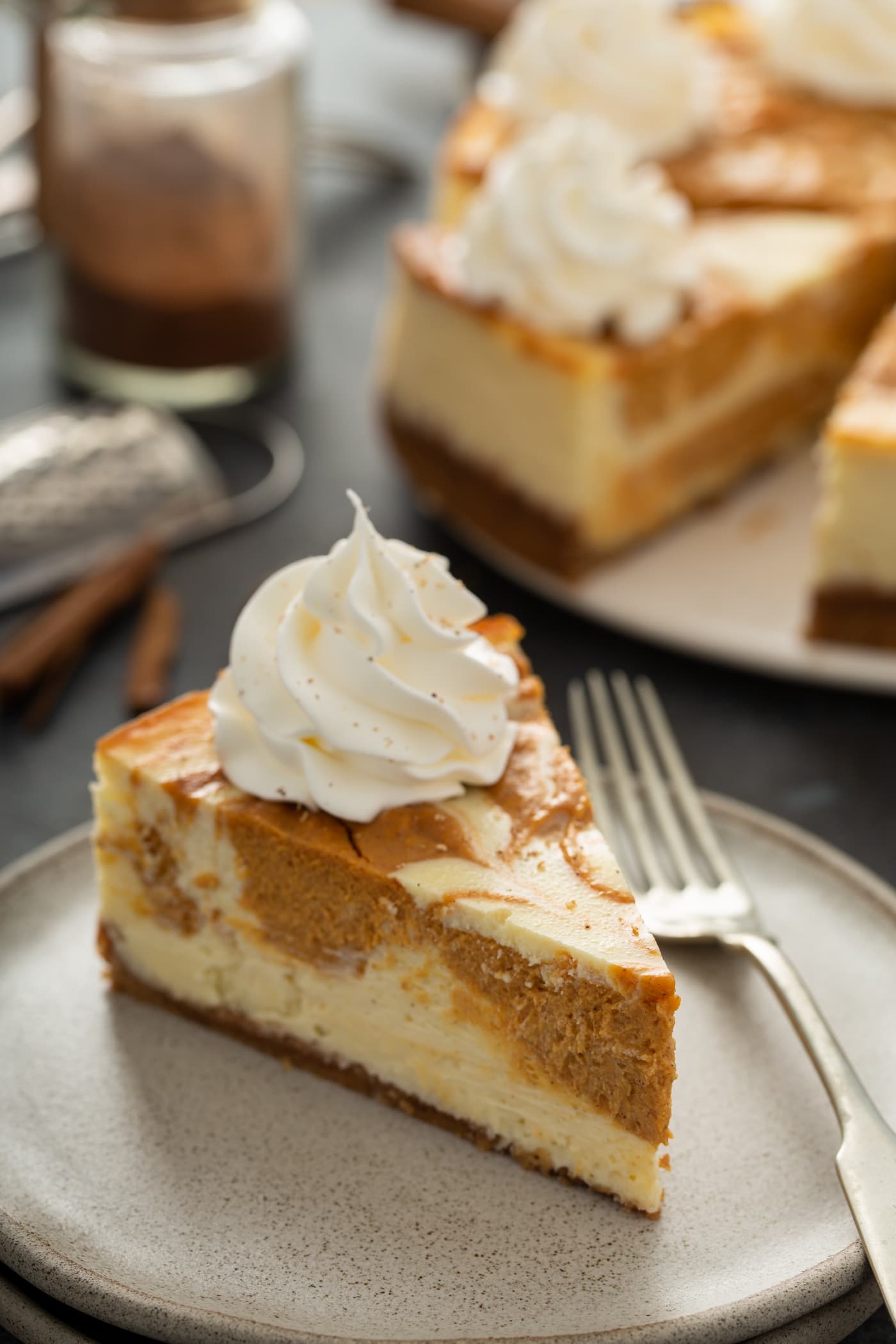 A slice of swirled pumpkin cheesecake on a plate with a fork. The rest of the cheesecake is in the background.