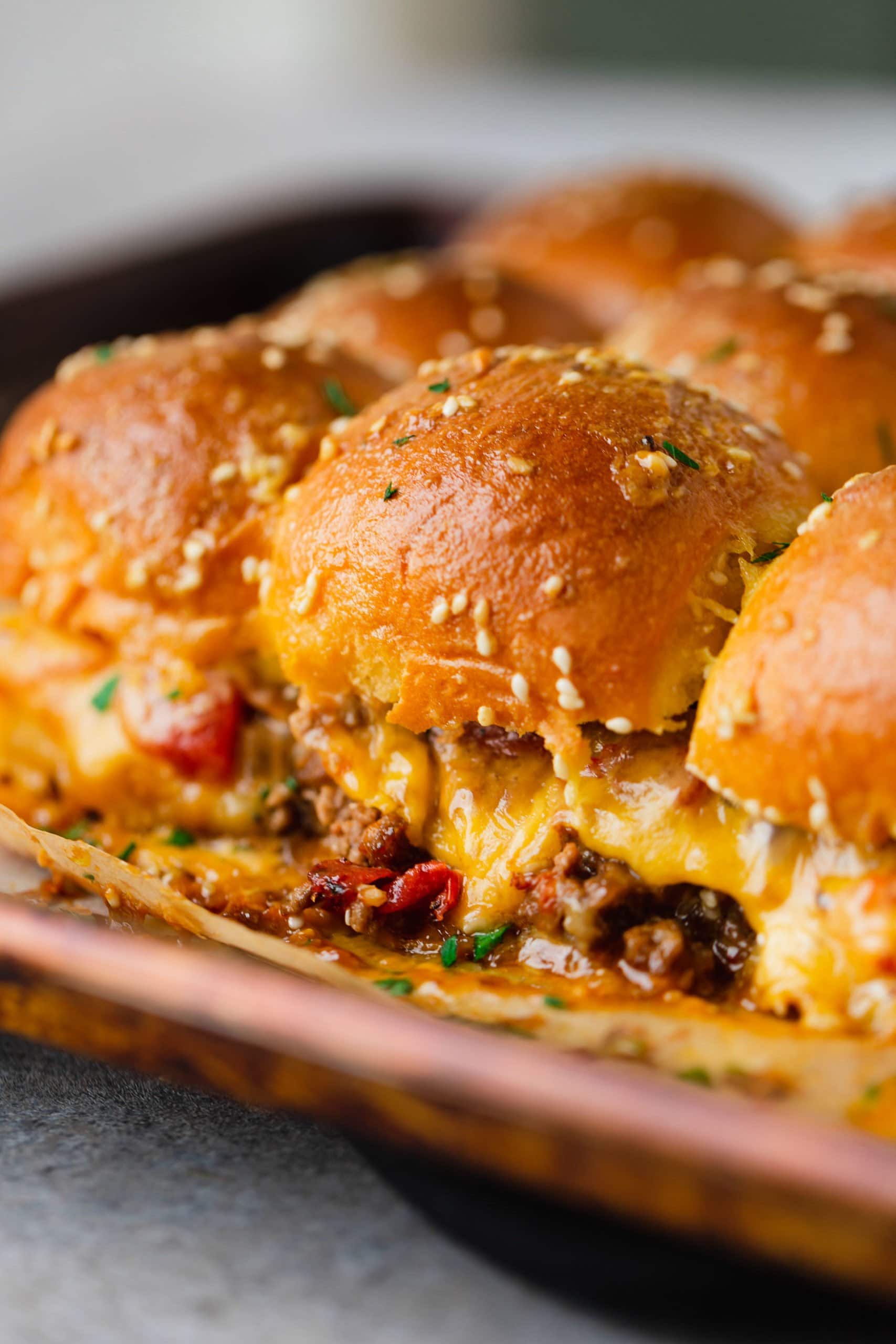 A plate of cheeseburger sliders. The cheese is oozing out from the buns.