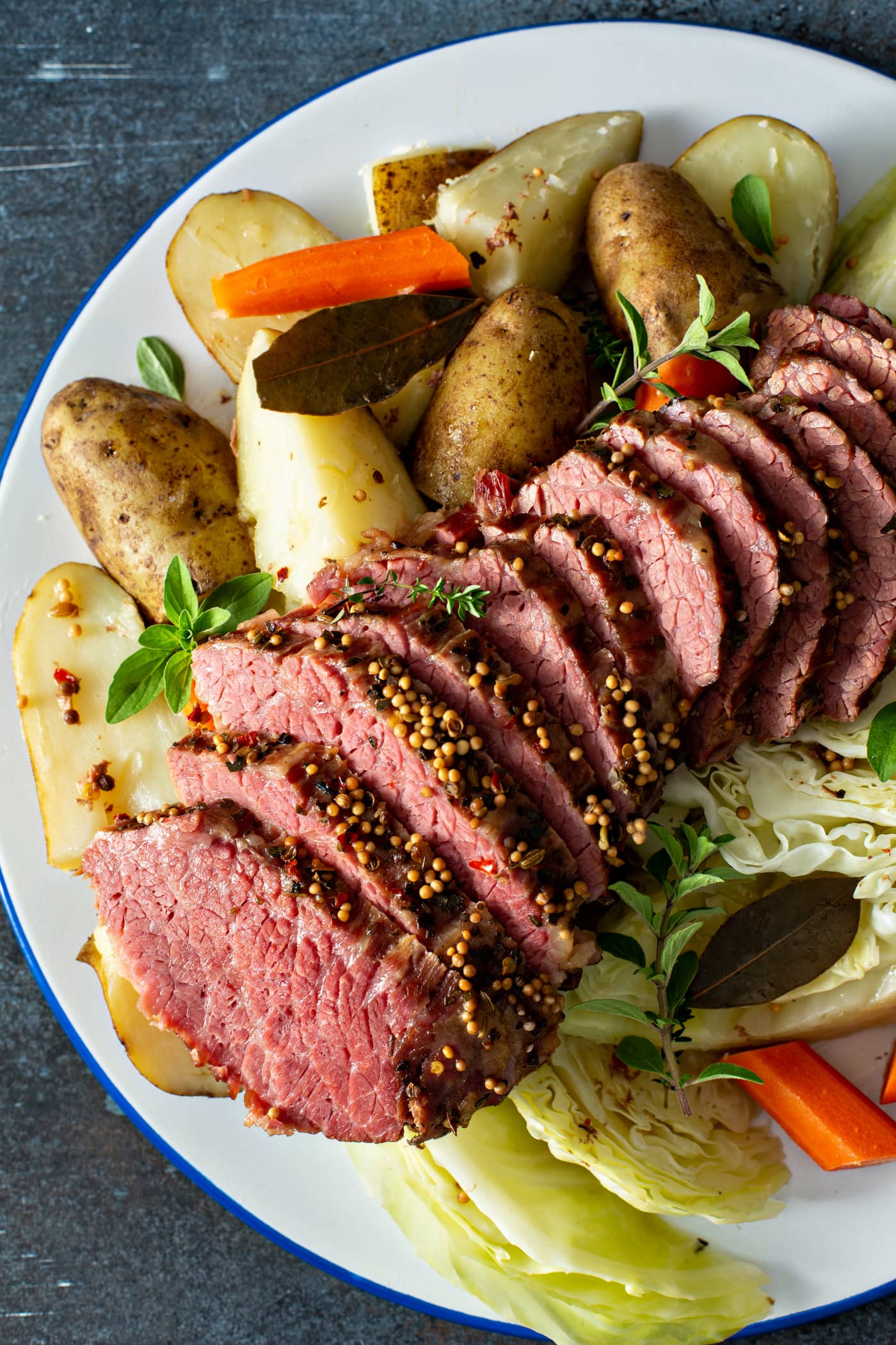A platter of corned beef and cabbage. There are 12 slices of corned beef with potatoes and carrots on one side and cabbage and carrots on the other side.