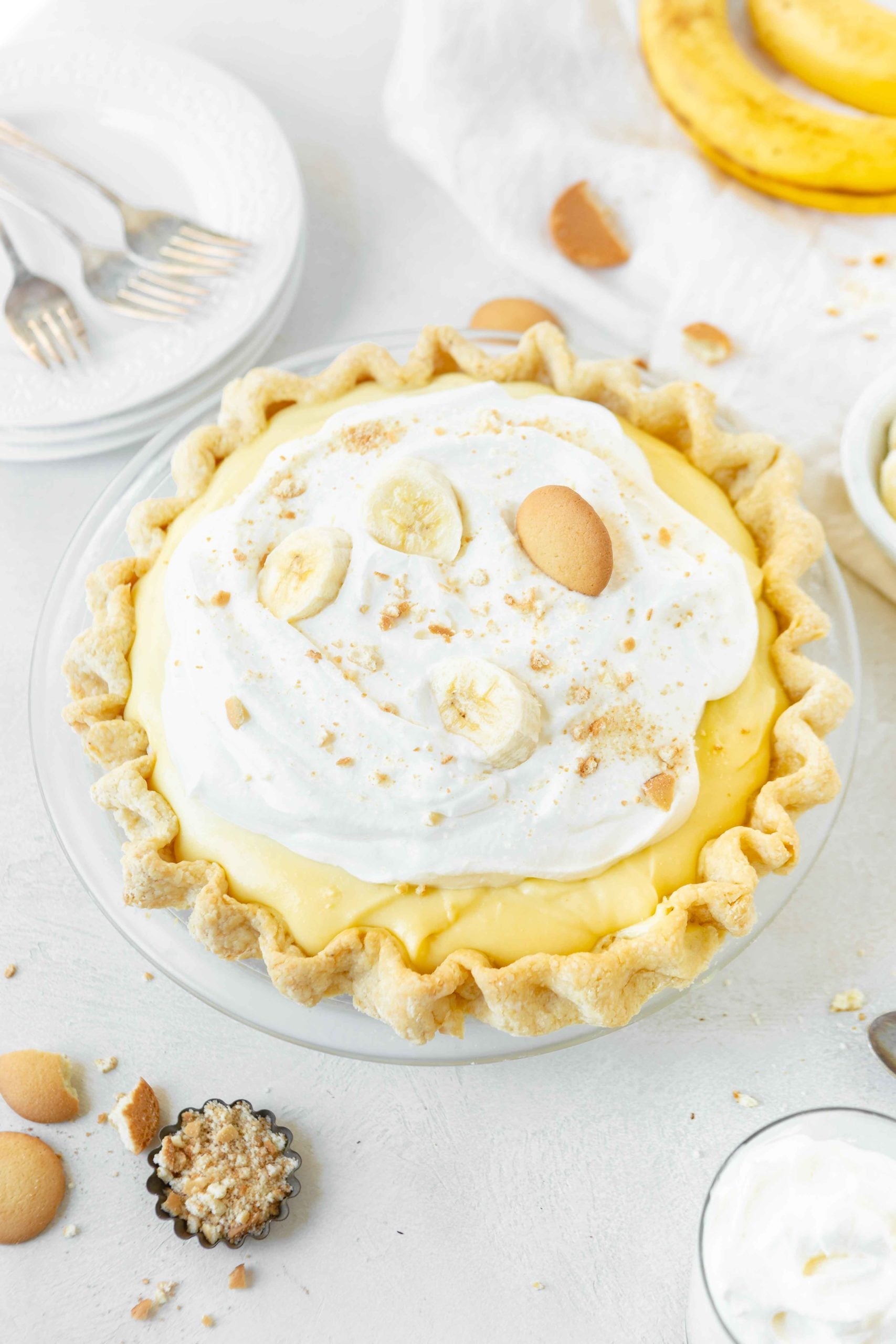 a photo of a homemade banana cream pie in a clear glass pie plate. The pie is topped with whipped cream, banana slices, and a Nilla Wafer.