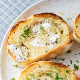 a photo of several slices of buttery toasted garlic bread sprinkled with chopped parsely sitting on a white plate