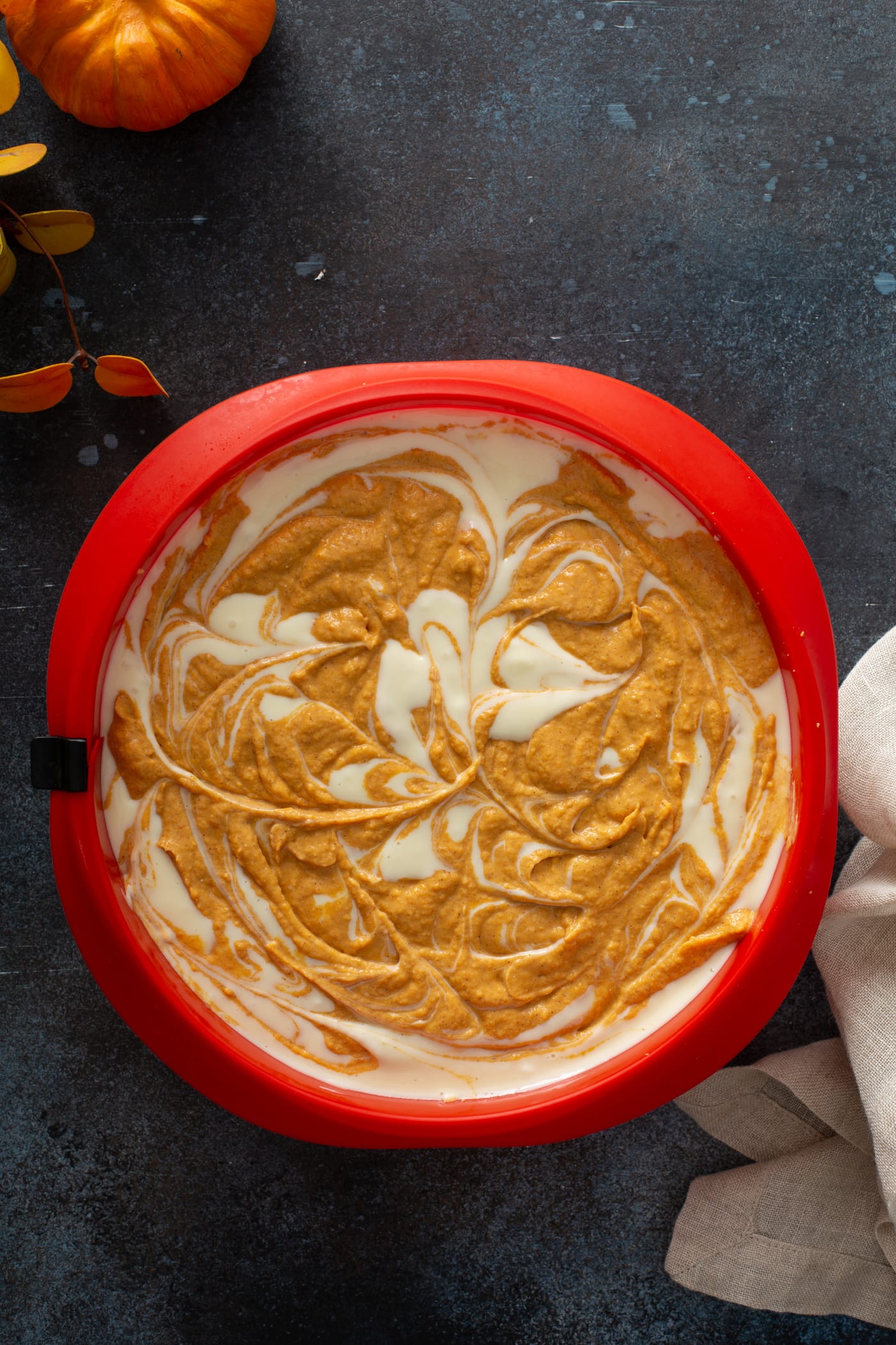 The cheesecake dish filled with cheesecake and pumpkin cheesecake filling that has been swirled together.