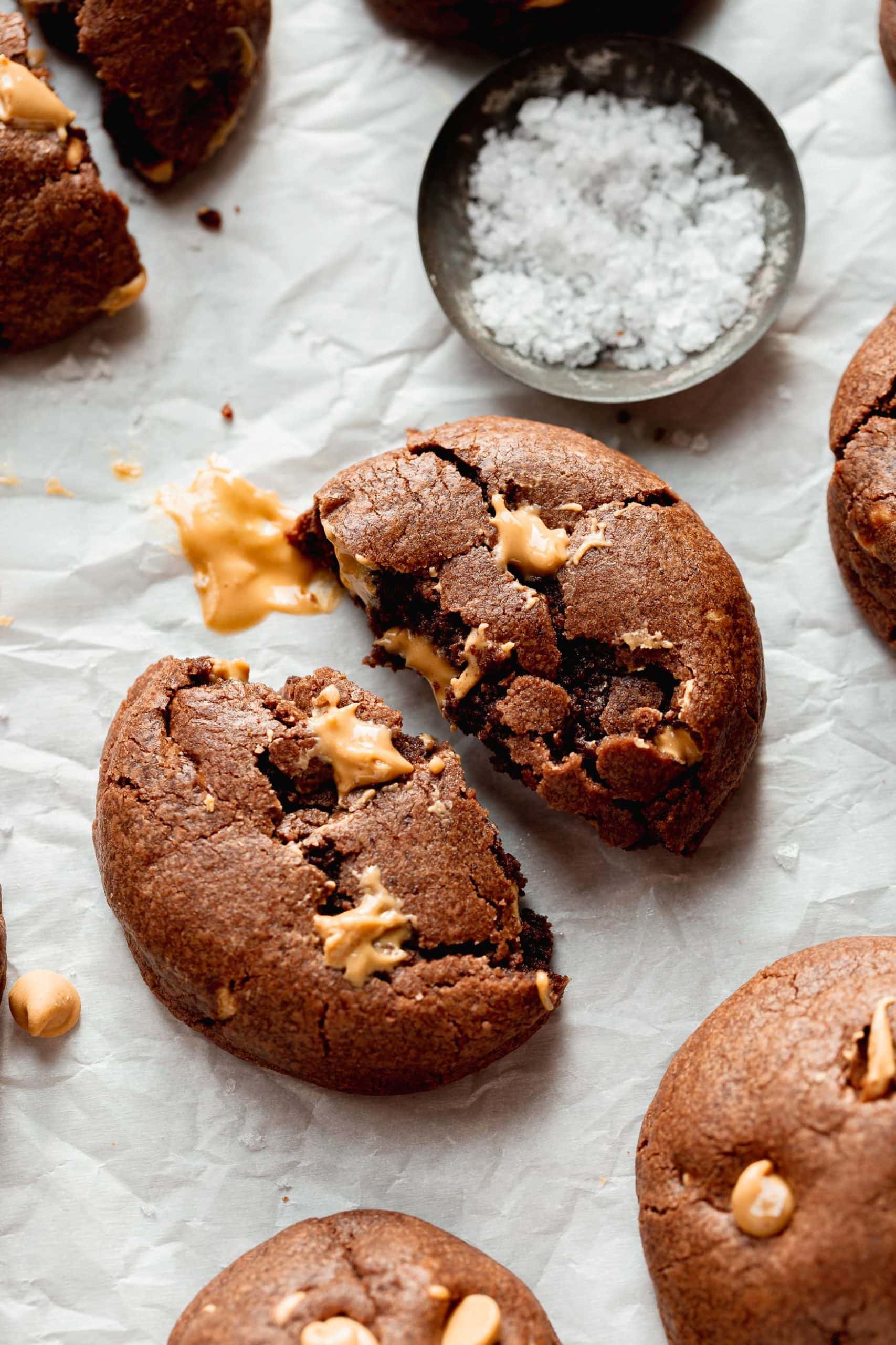 A peanut butter chocolate cookie that is broken in half. The chocolate cookie has peanut butter chips in it.