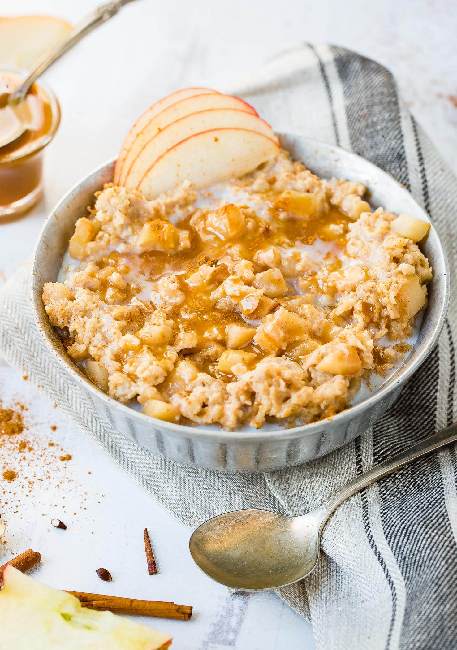 A photo of a bowl of oatmeal full of apple chunks and topped with caramel drizzle and thinly sliced apples