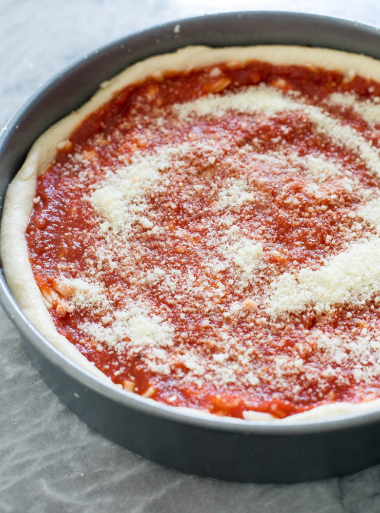 Deep dish pizza in a pan getting ready to be baked. 