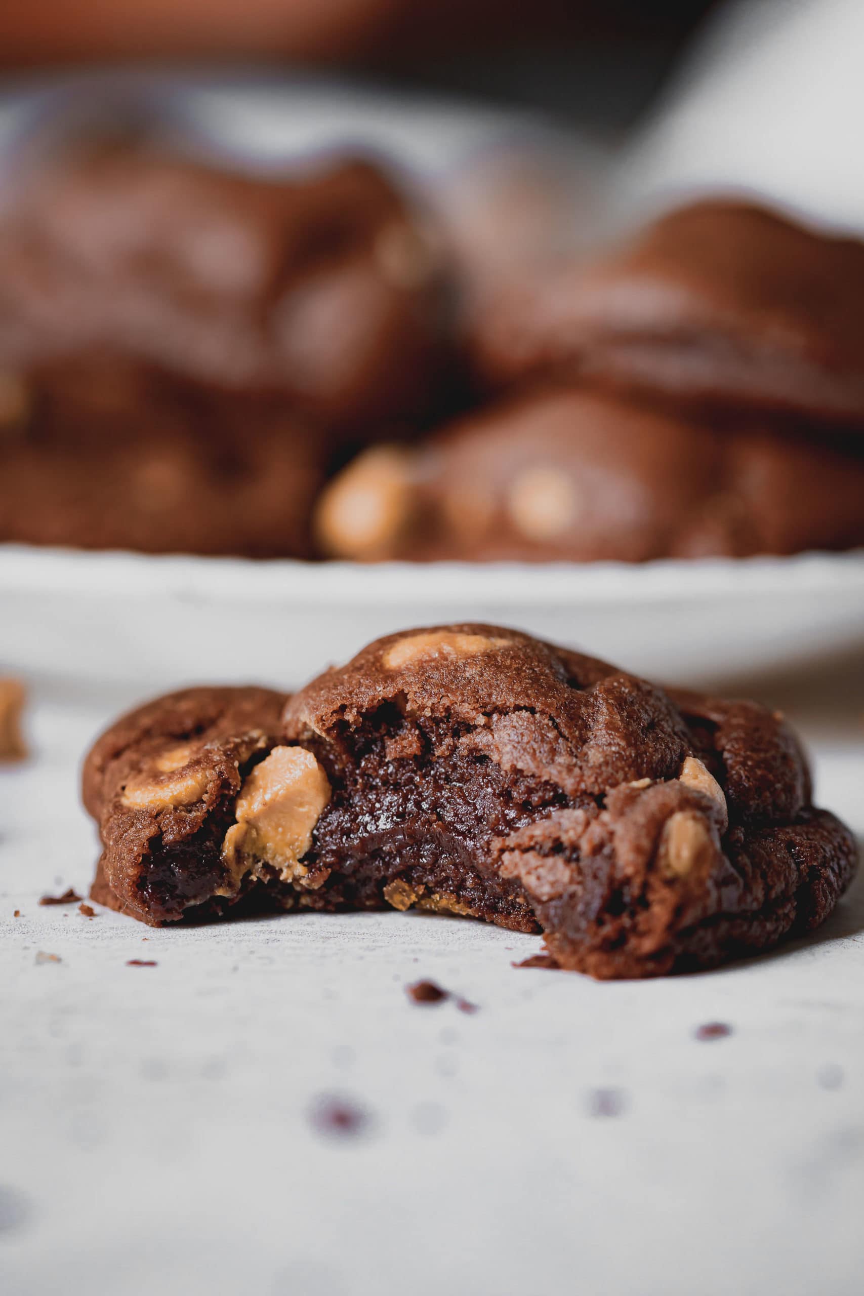 A peanut butter chocolate cookie that is broken in half. The chocolate cookie has peanut butter chips in it.