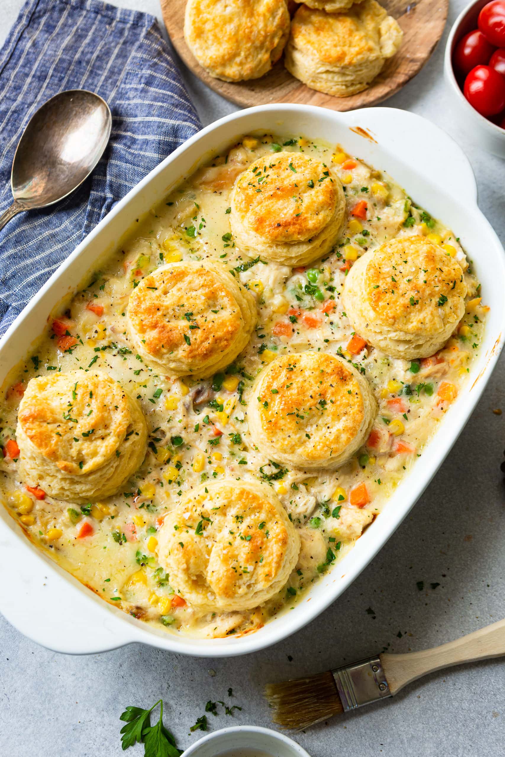 a photo of a white rectangular baking dish full of creamy chicken pot pie filling with six golden butter milk biscuits on top.