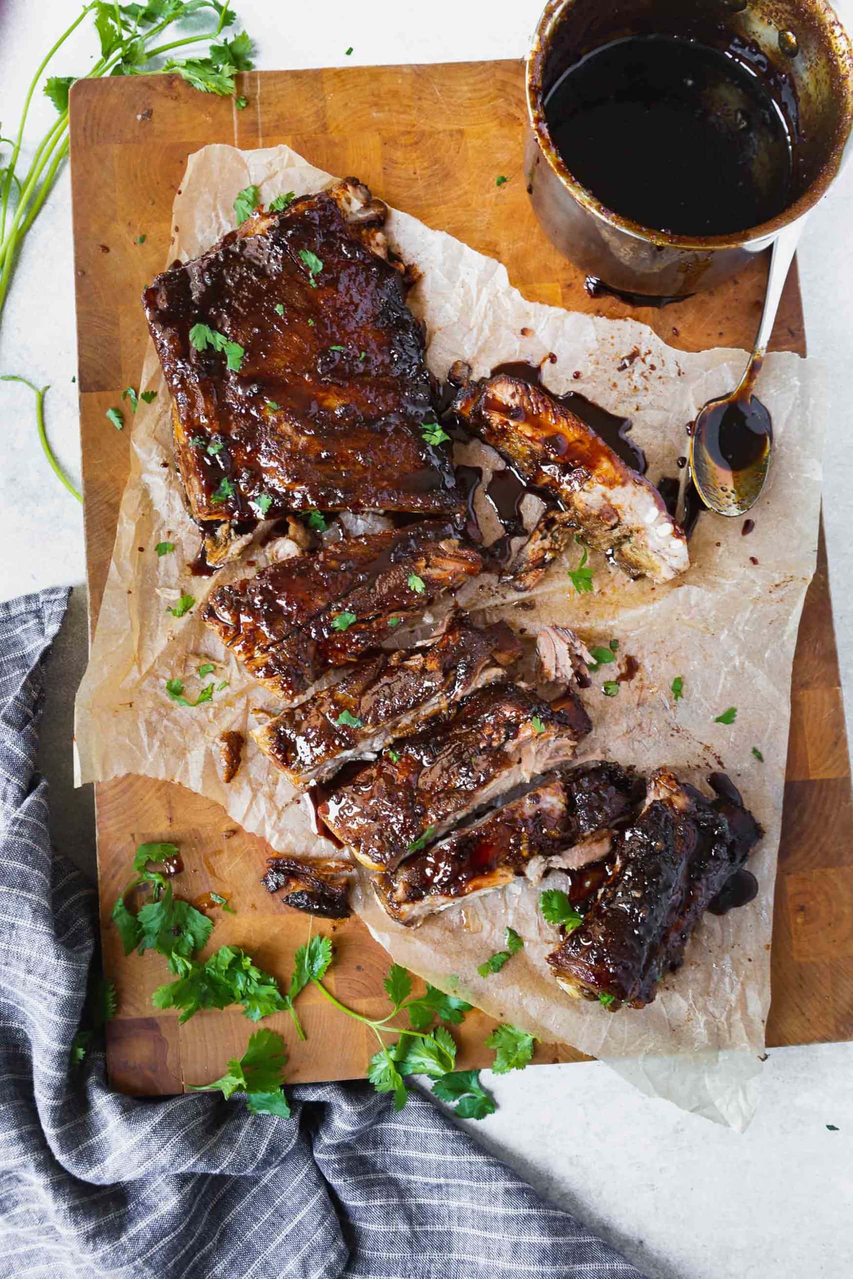 a photo of a rack of ribs sitting on piece of parchment paper with about half of the ribs cut off from the rack and cut into individual ribs. they are all covered in a sticky asian sauce.