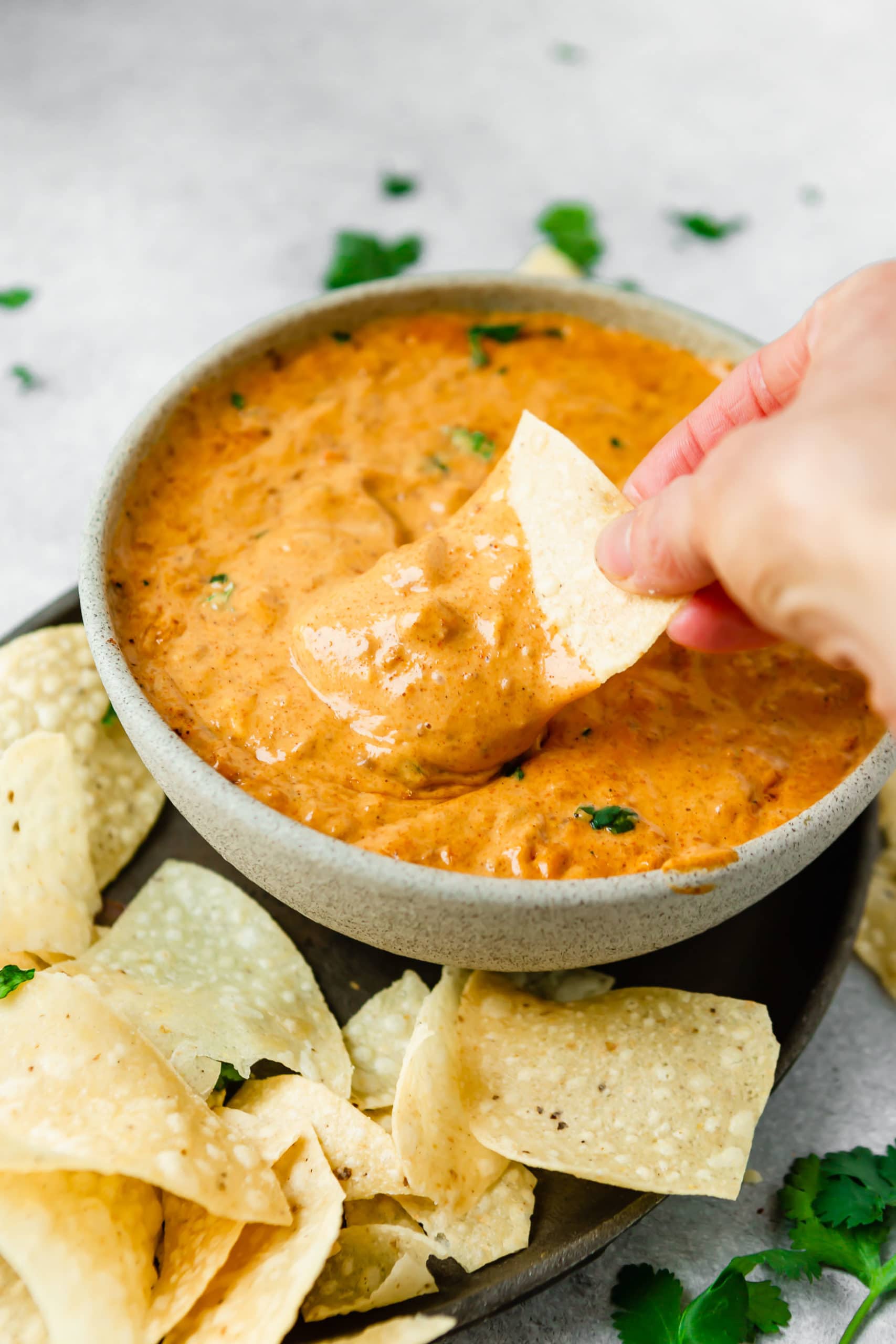 A bowl of queso dip. It is thick and cheesy and a tortilla chip is being dipped into the queso dip.