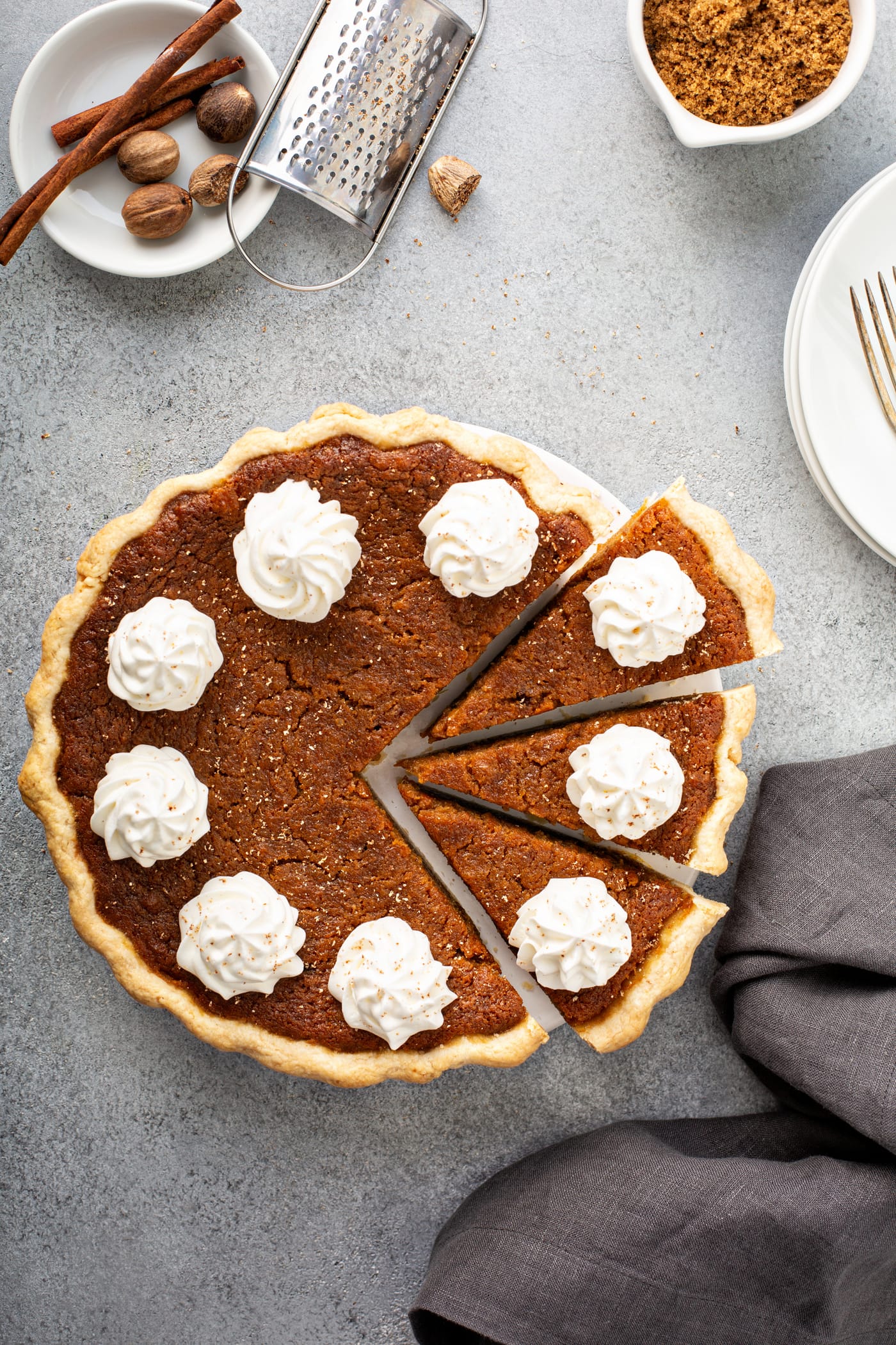 A photo of a baked sweet potato pie covered in dollops of whipped cream with three slices pulled out.