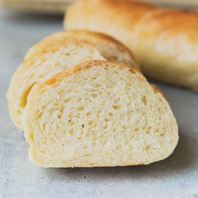 a photo of a slice of french bread leaning up against more slices of french bread with a full loaf in the background