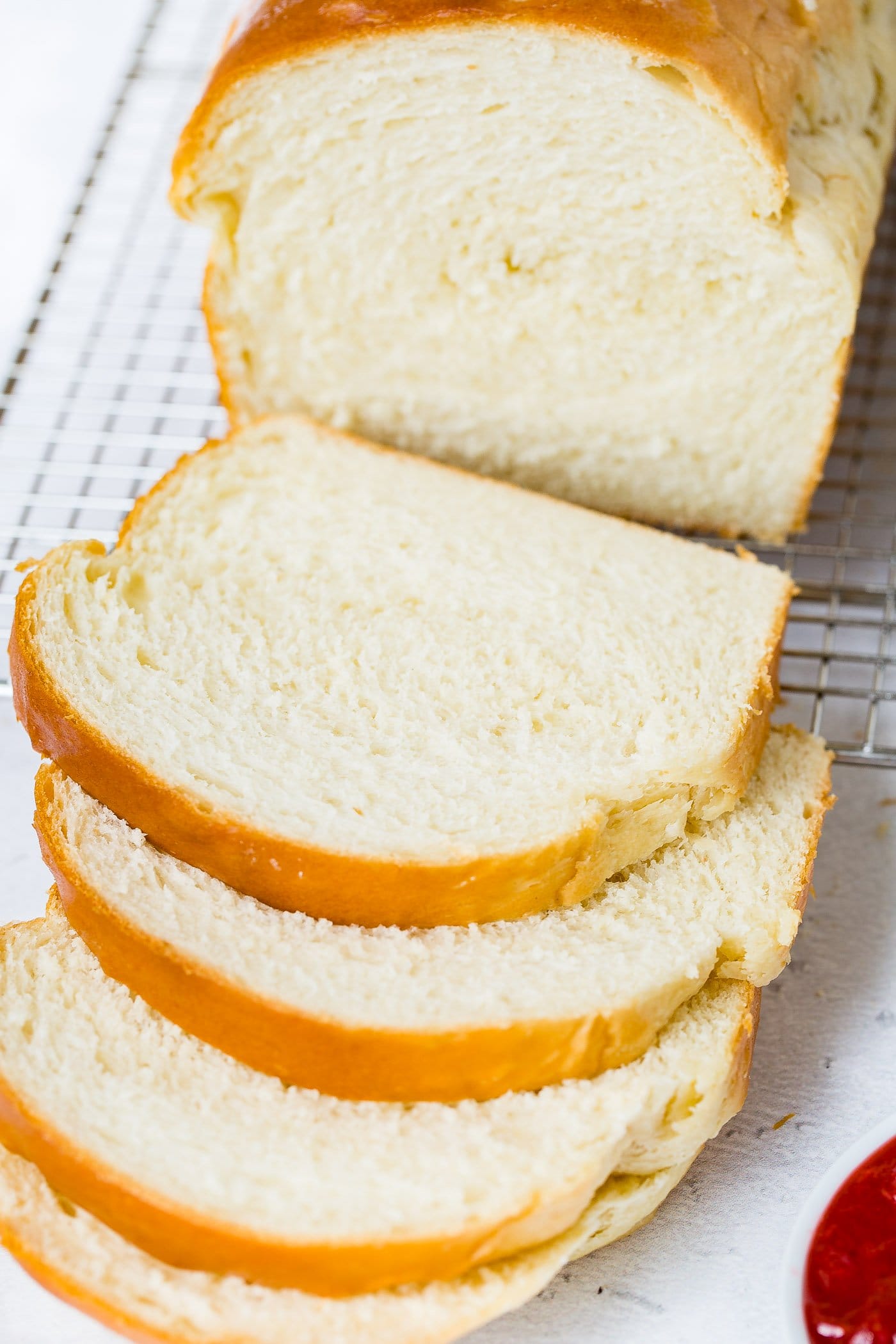 A loaf of homemade white bread with three slices that have been cut. The bread is golden brown on top. It is on a wire cooling rack.
