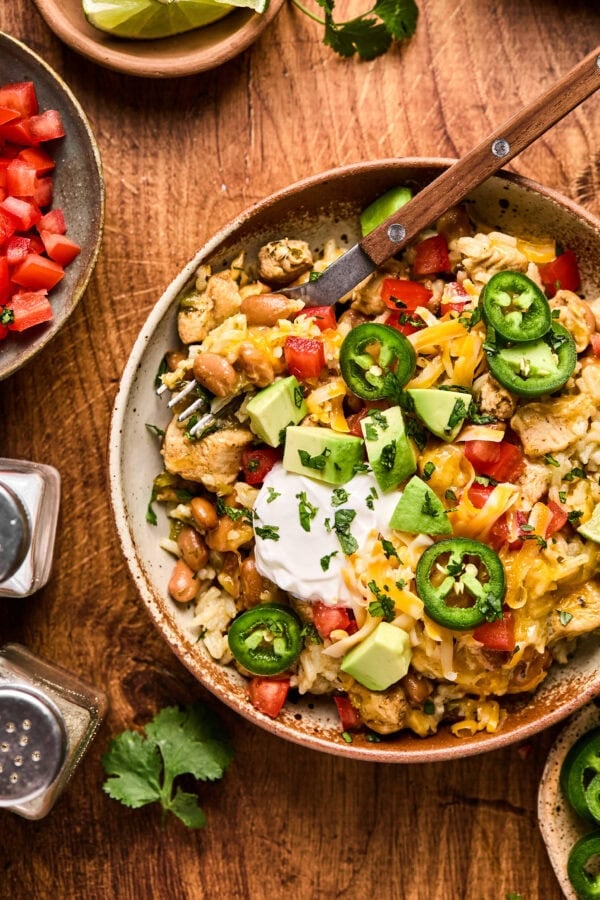 a photo of a bowl of cilantro lime chicken burrito bowl topped with melted cheese, sour cream and sliced jalapenos