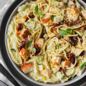 a photo of creamy chicken pasta topped with sun dried tomatoes, golden chicken chunks and fresh basil.