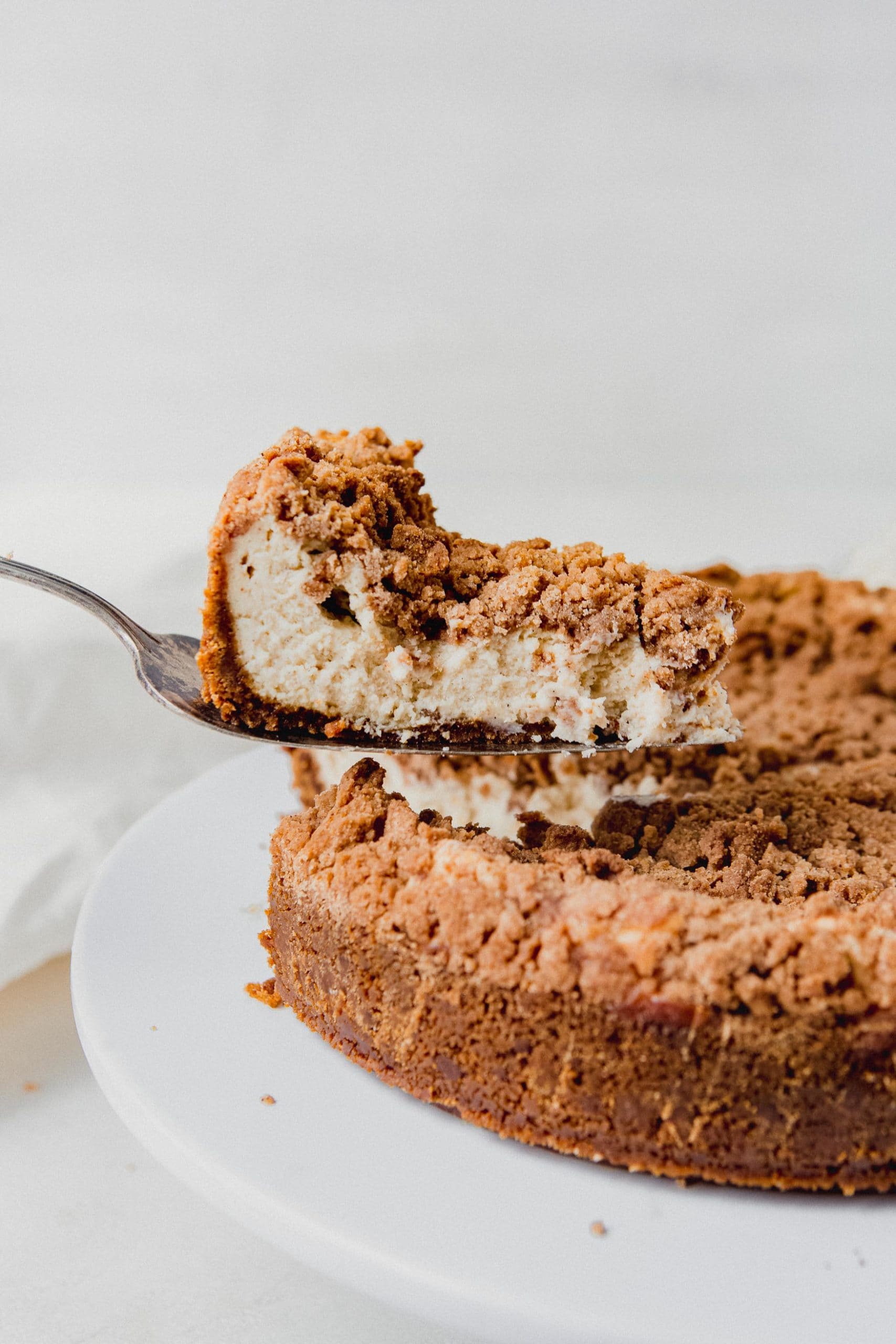 A slice of biscoff snickerdoodle cheesecake being lifted on a pie server. You can see the cinnamon sugar snickerdoodle topping on the creamy cheesecake.