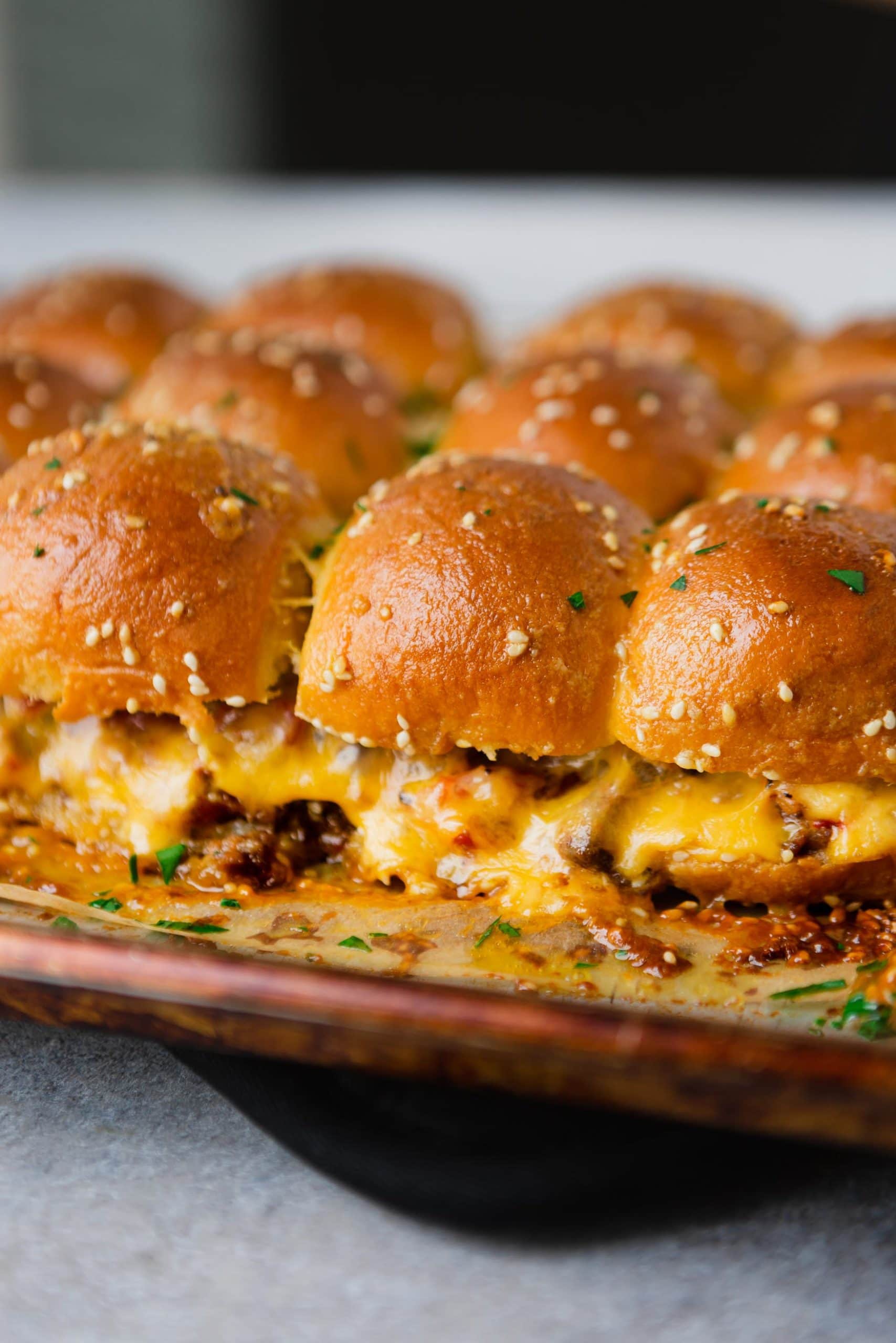 A pan of cheeseburger sliders. There is hamburger, and melted cheese on golden dinner rolls.