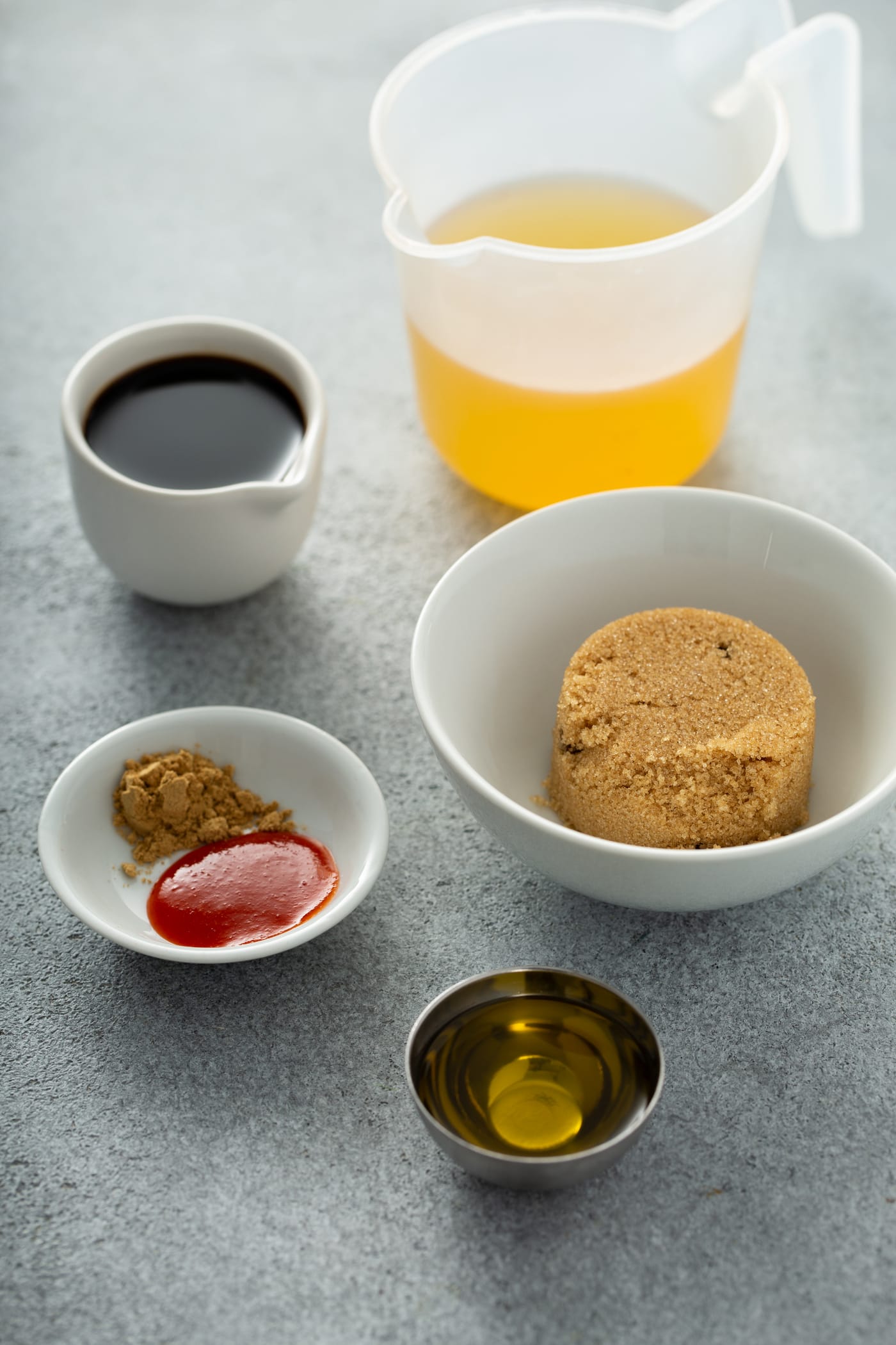 A photo of all the ingredients in separate dishes to make the sauce for beef and broccoli, including beef broth, soy sauce, brown sugar, ground ginger, sriracha sauce, and sesame oil.