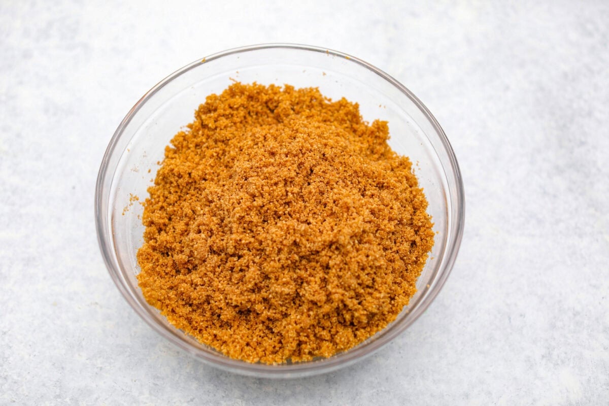 Graham cracker crumbs, spices, and butter mixed together in a glass bowl.  