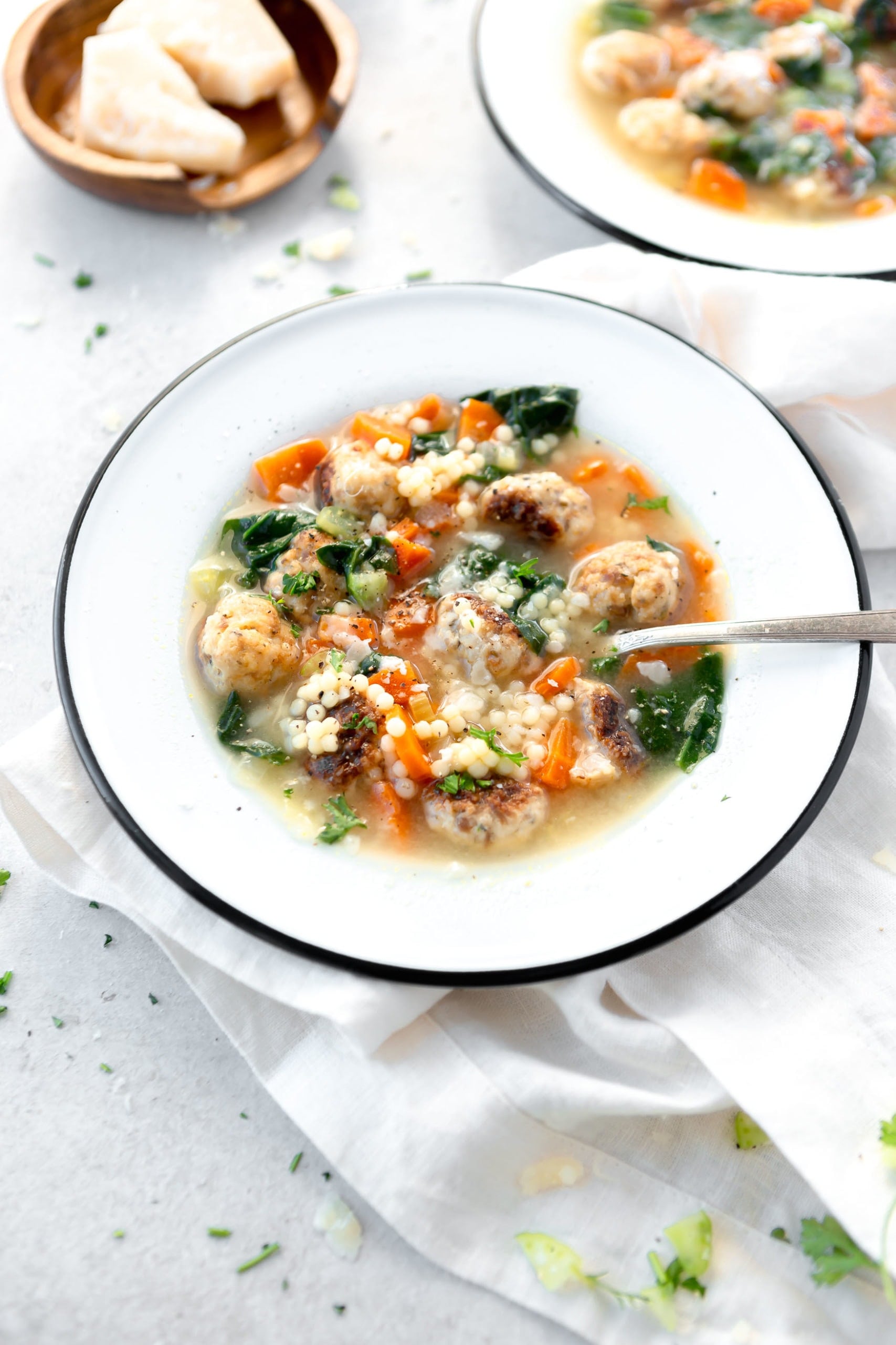 A bowl of Italian Wedding soup with a spoon in it. The soup is packed with meatballs and carrots and spinach.