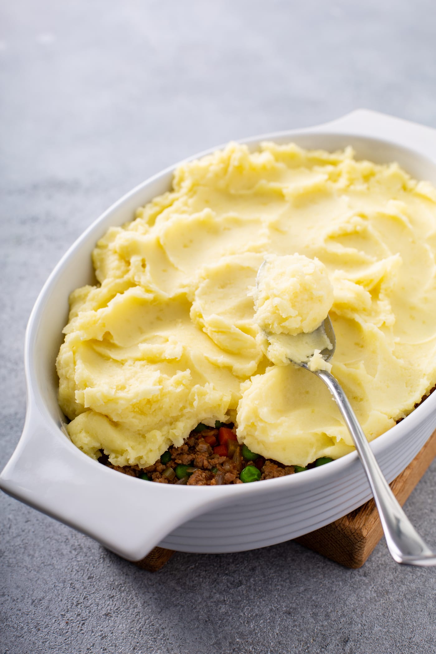 A casserole dish filled with shepherd's pie filling and topped with mashed potatoes. There is a spoon resting on top.