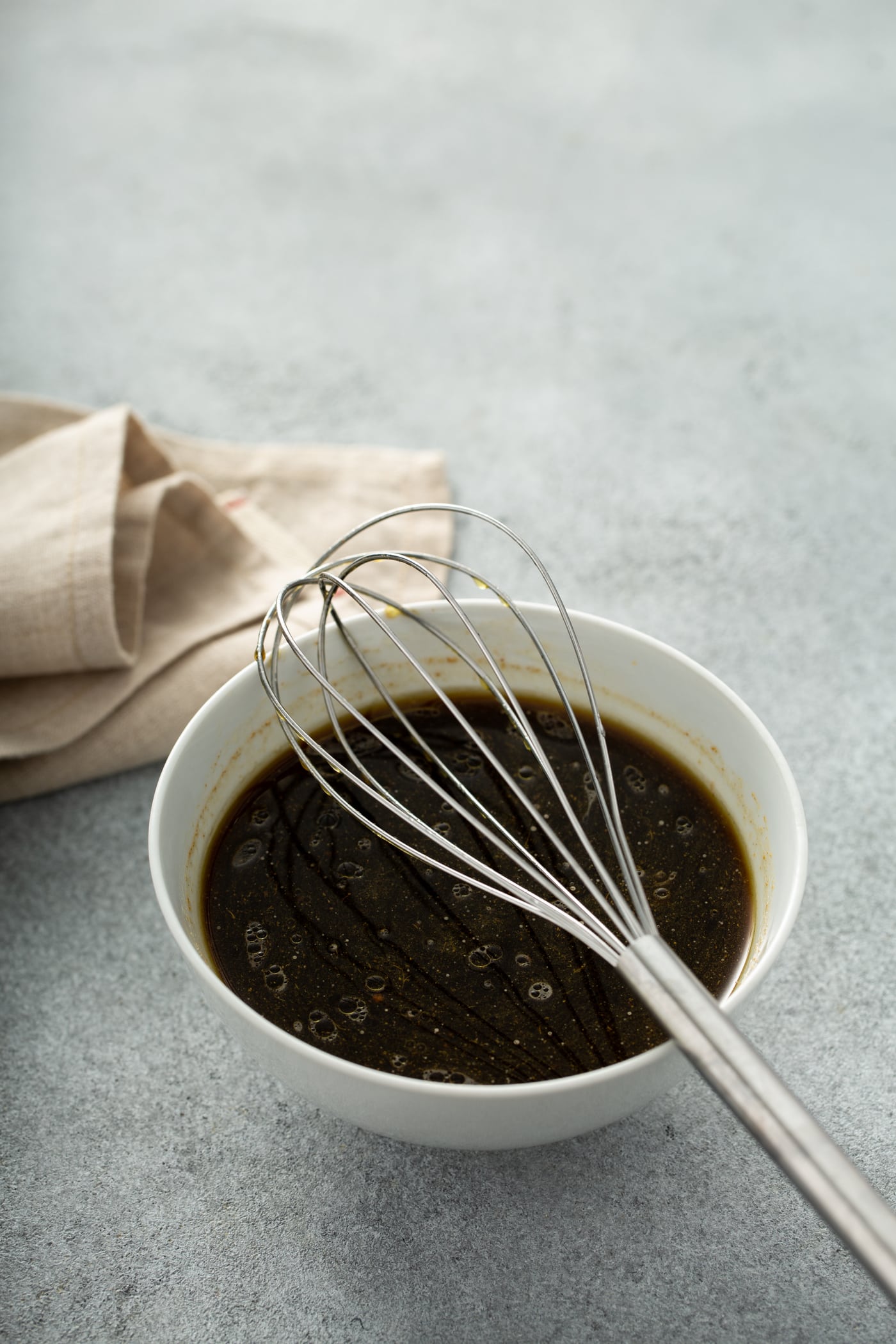 A photo of the sauce for beef and broccoli all whished together in a white bowl with a wire whisk sitting on top of the bowl.