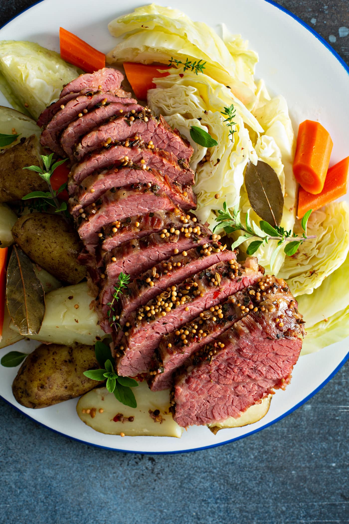 A serving tray of sliced corned beef with potatoes and carrots on one side and cabbage and carrots on the other side.