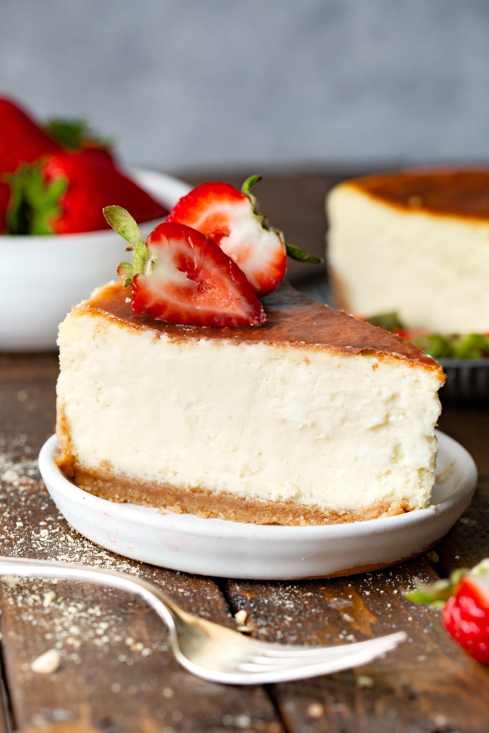 a photo of a large slice of classic cheesecake taken from the side so you can see the cross-section. It has a thick graham cracker crust and golden top with berries