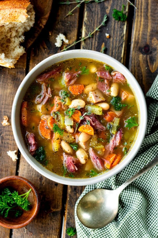 a photo of a large bowl of ham and bean soup with a large chunk of crusty bread next to it and a spoon a photo of a large bowl of ham and bean soup with a large chunk of crusty bread next to it and a spoon