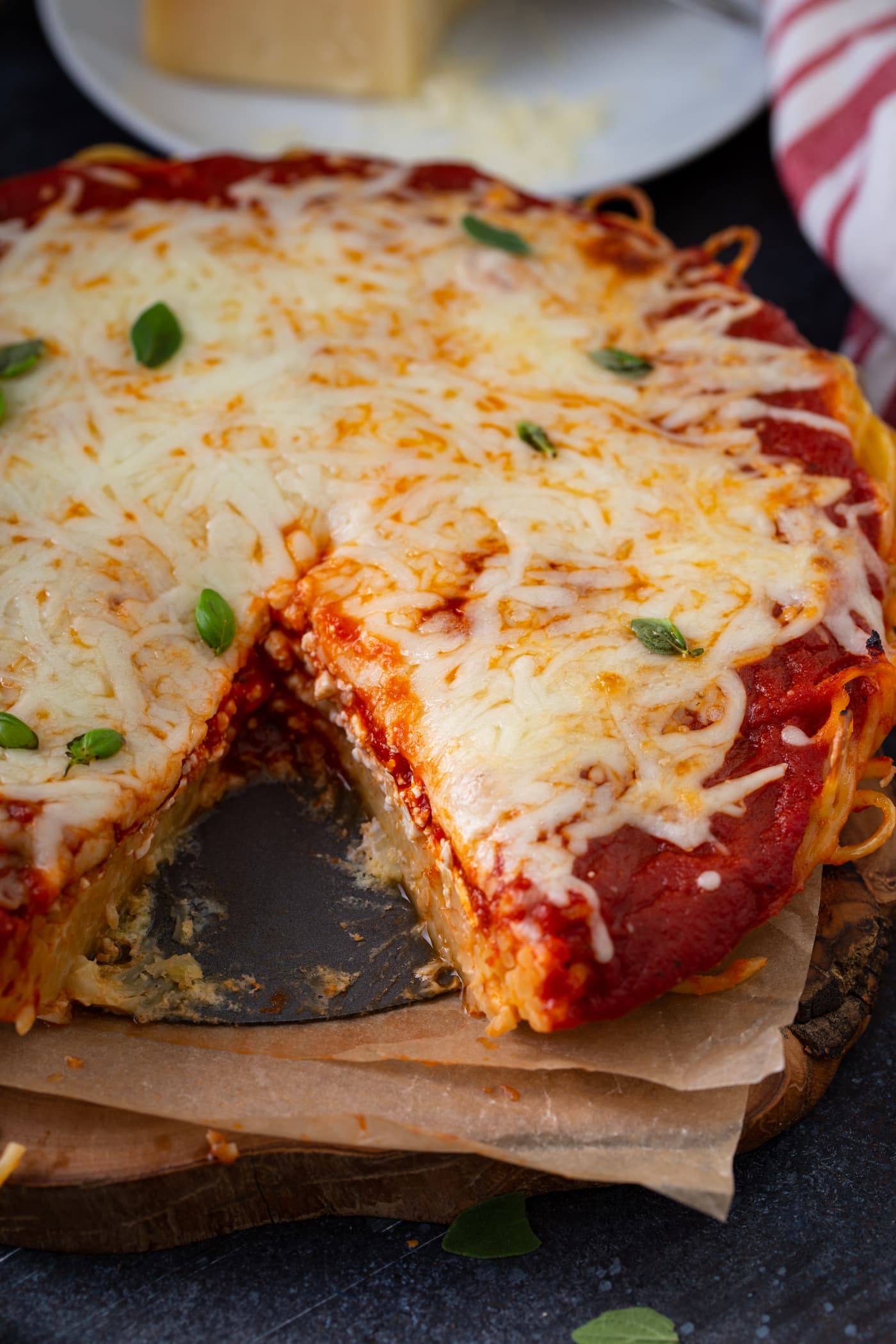 A baked spaghetti pie that has a slice removed. There are layers of spaghetti, spaghetti sauce, and melted shredded cheese. A little fresh basil is sprinkled on top.