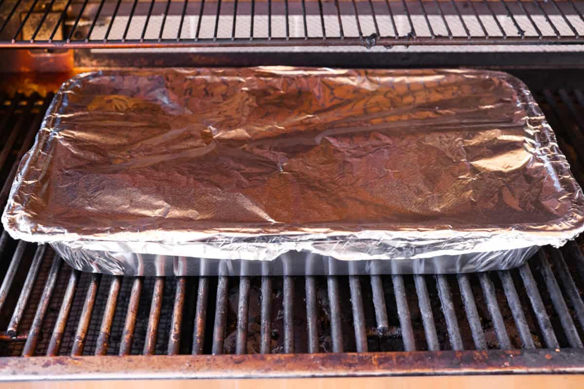 Ribs in a disposable aluminum pan covered and on the grill.