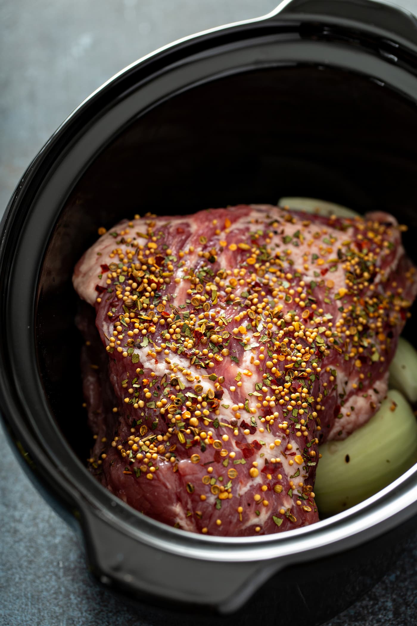 A slow cooker with potatoes and cabbage in the bottom and a corned beef resting on top.