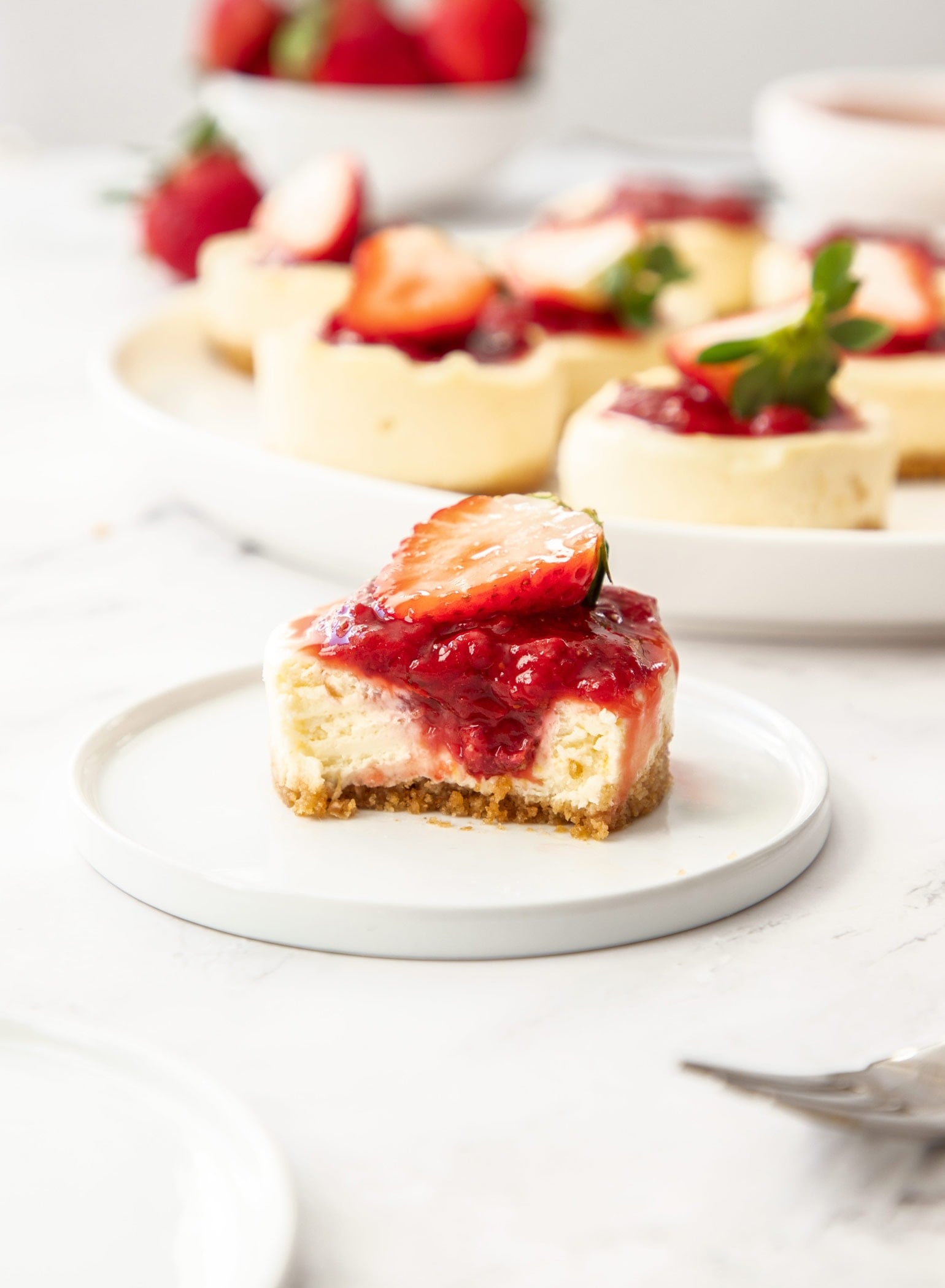 A mini cheesecake on a small white plate, with more in the background