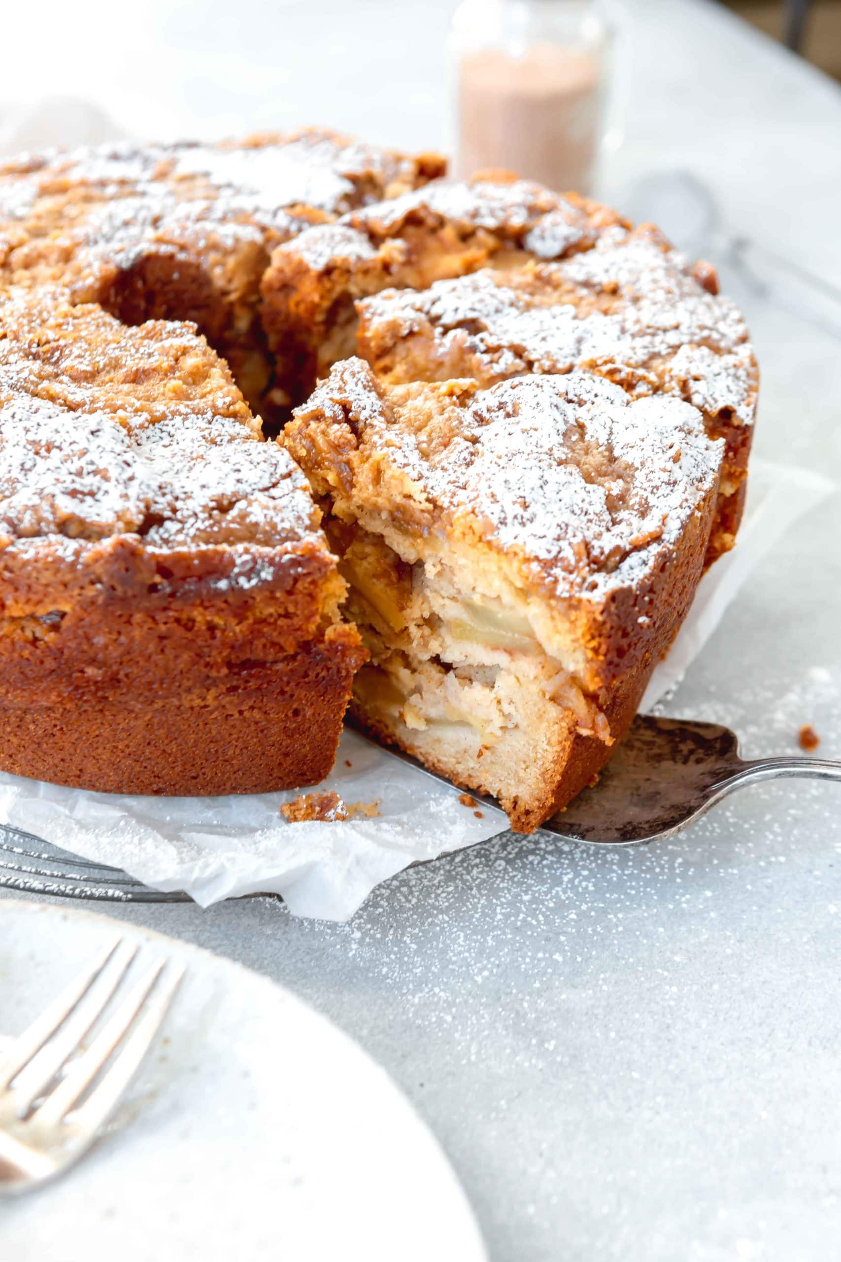 A Jewish apple cake with a couple of slices cut. You can see slices of apples and powdered sugar on top.