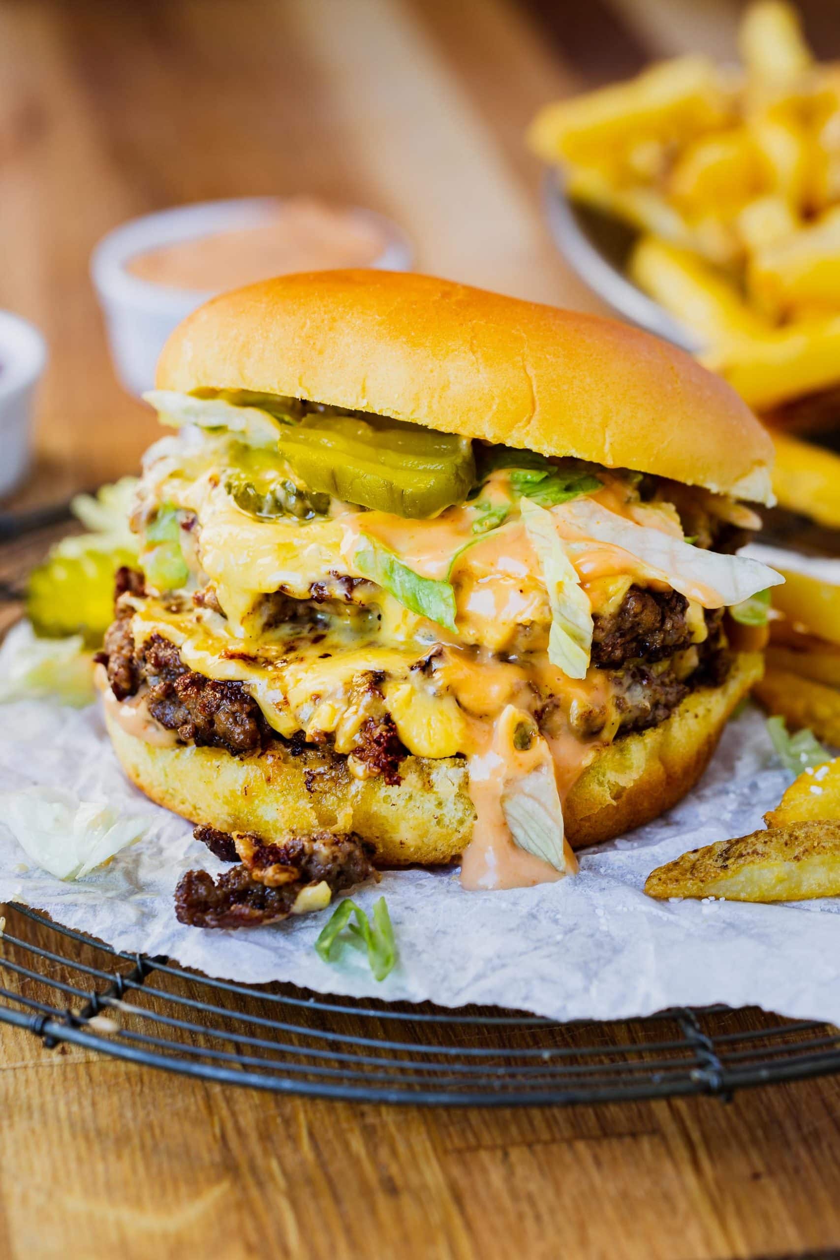 a photo of a juicy smash burger with two cheesy patties, pickles and shredded lettuce on a golden toasted bun with a side of fries.