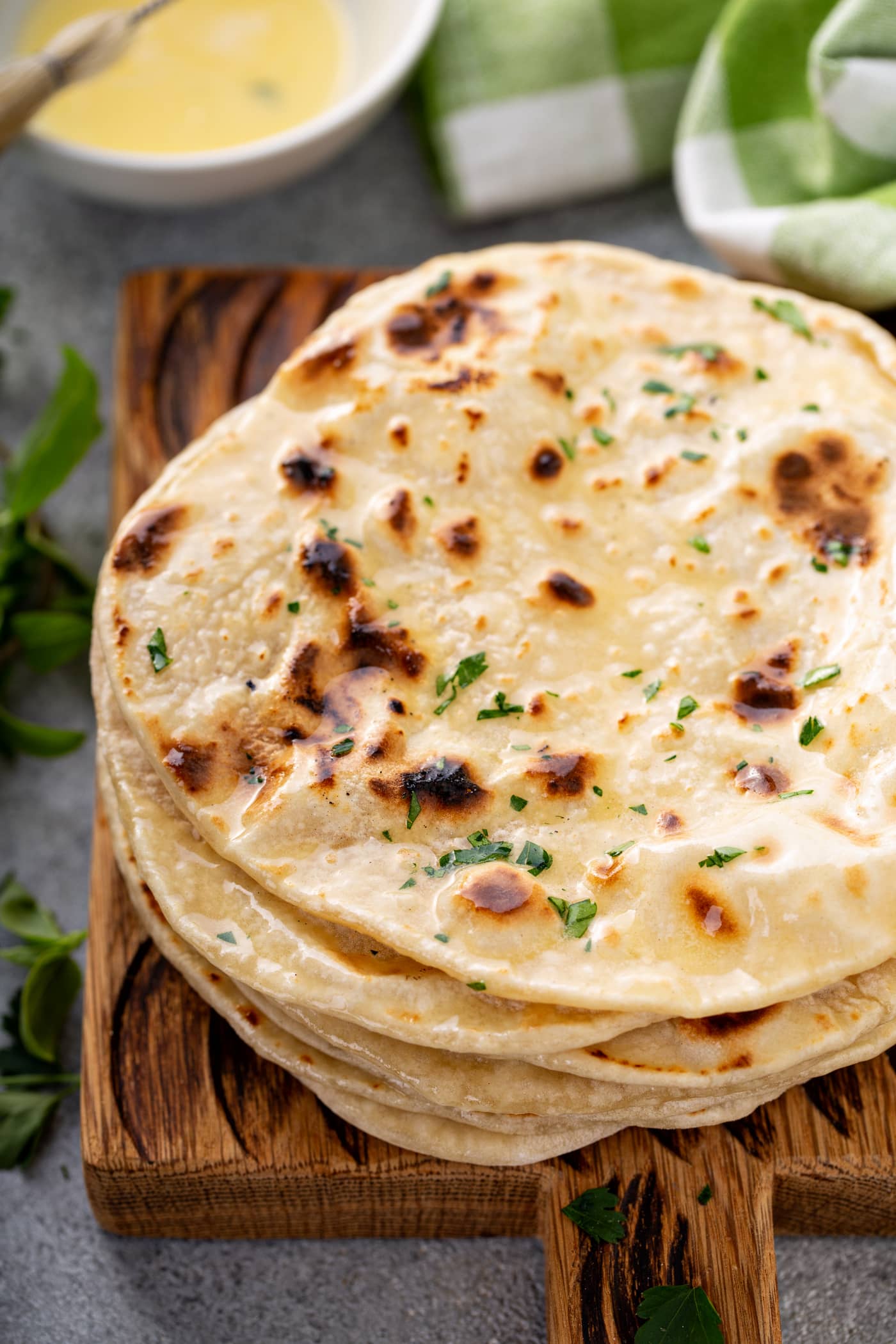 A photo of a stack of cooked discs of unleavened bread topped with melted butter and chopped fresh parsley.