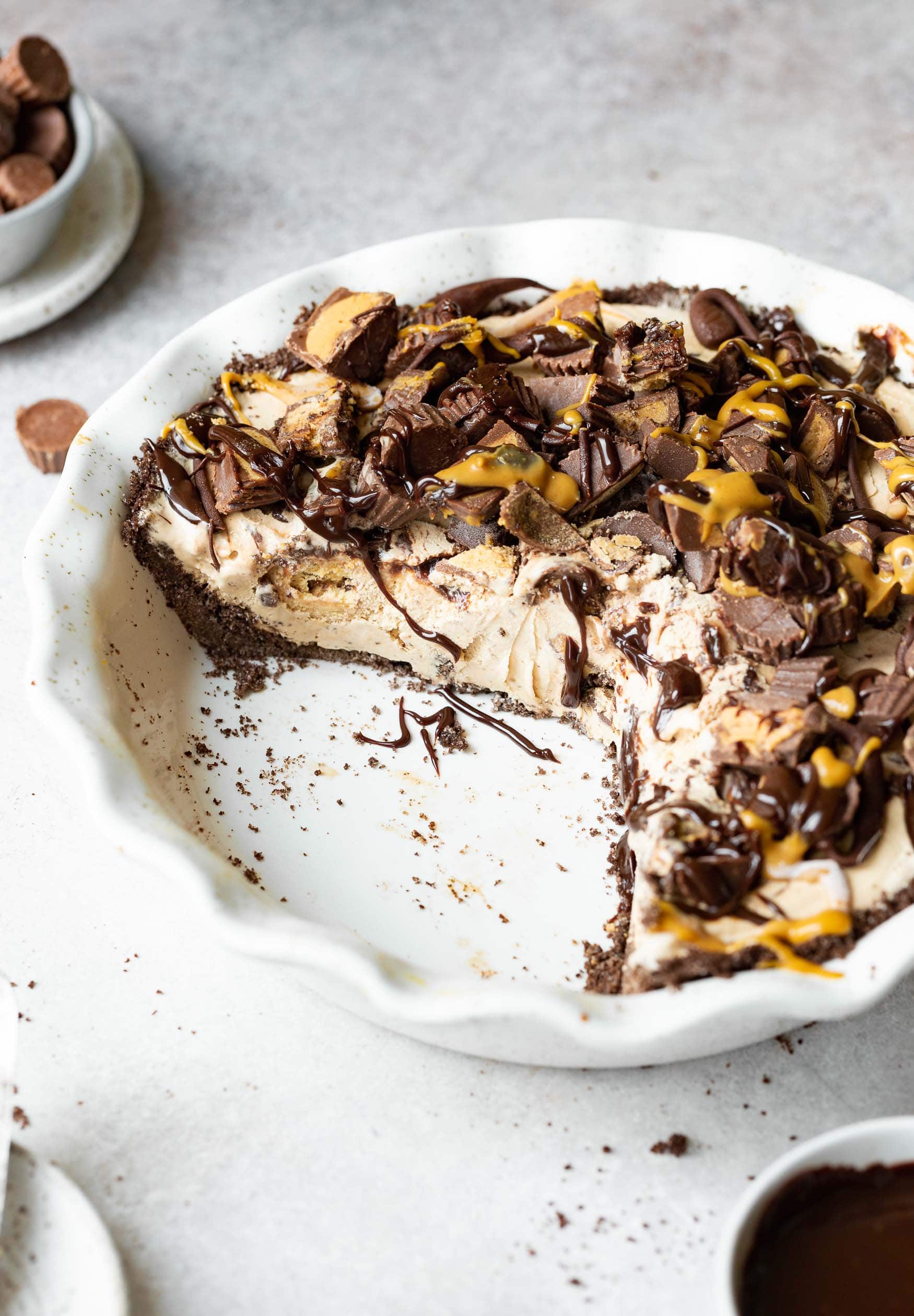 a photo of a reeses peanut butter ice cream pie in a white pie dish with several piece of pie missing.