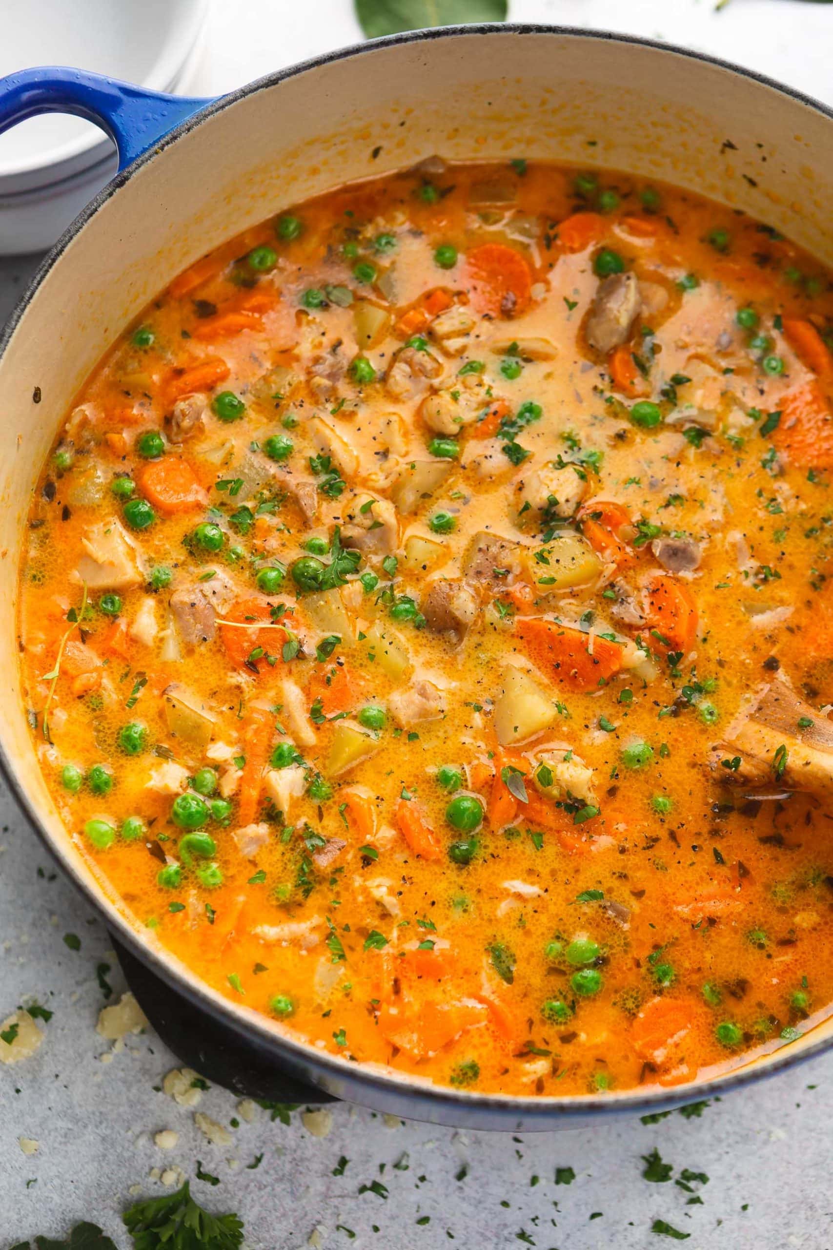 A pot of slow cooker chicken stew. There are bits of vegetables, chicken, and herbs in a reddish yellow gravy.
