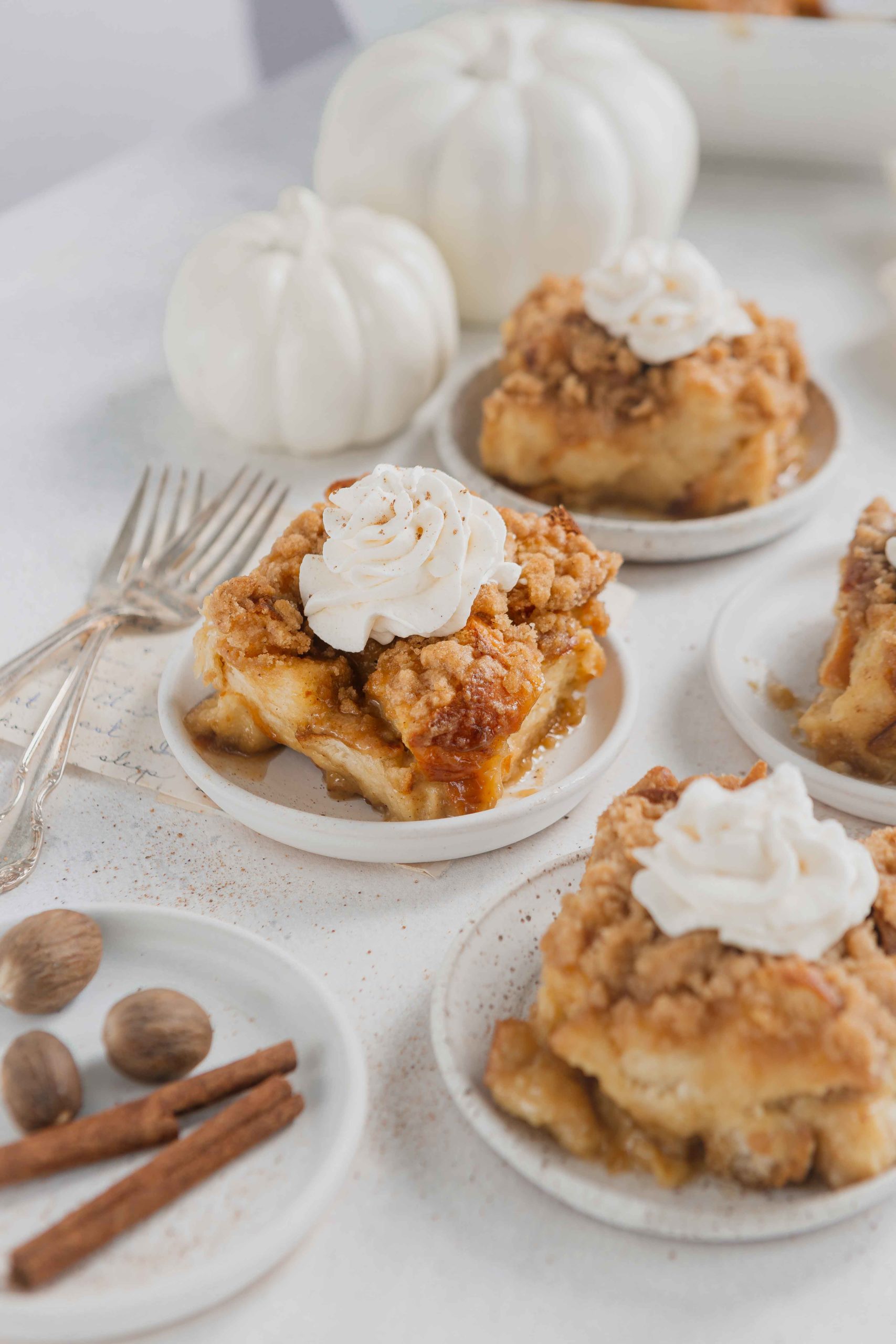 Servings of eggnog French toast casserole on white plates. The casserole is topped with a dollop of fresh whipped cream.
