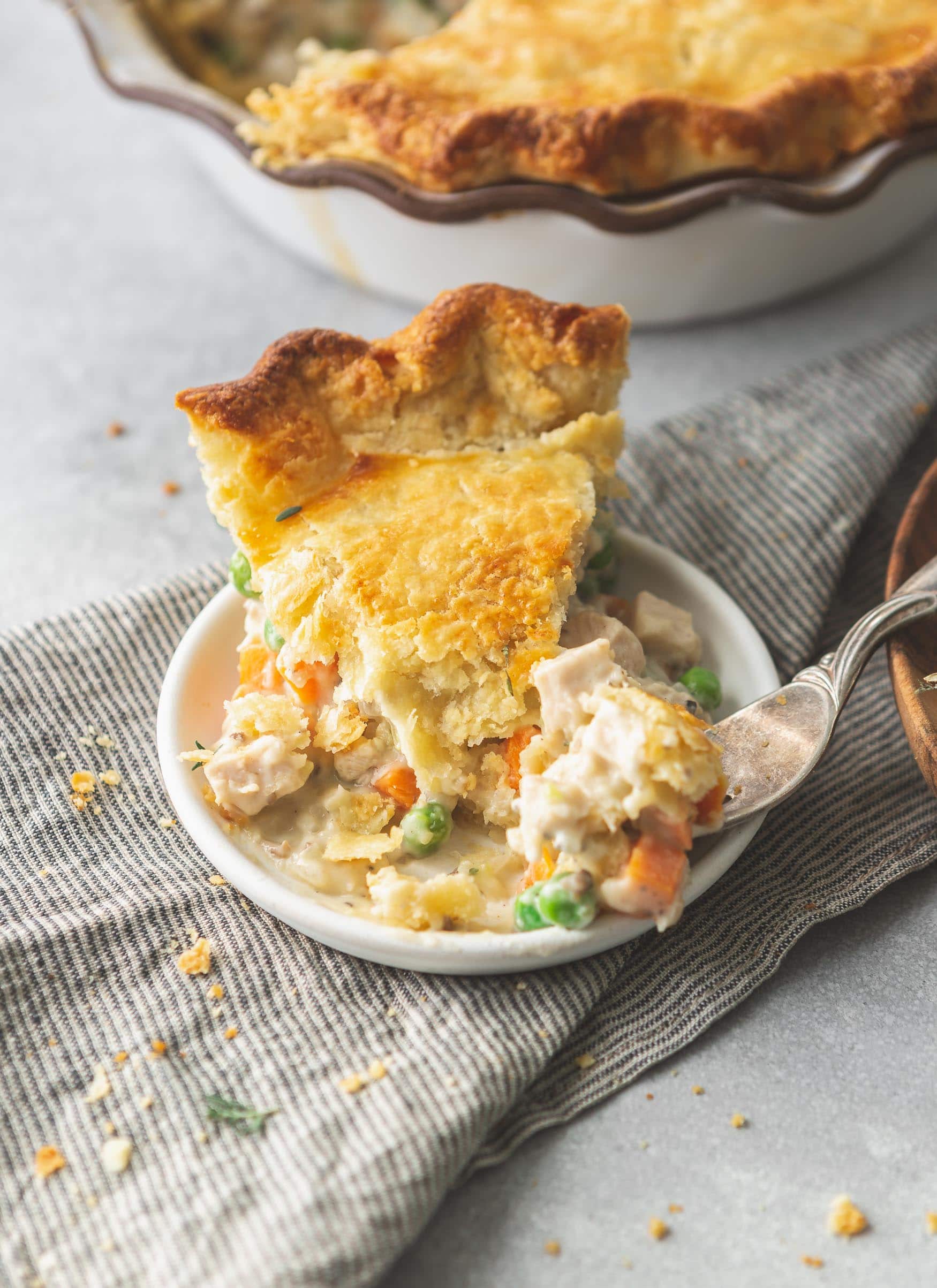 A slice of turkey pot pie on a small plate. The crust is golden brown and the filling is creamy and contains carrots and pies.