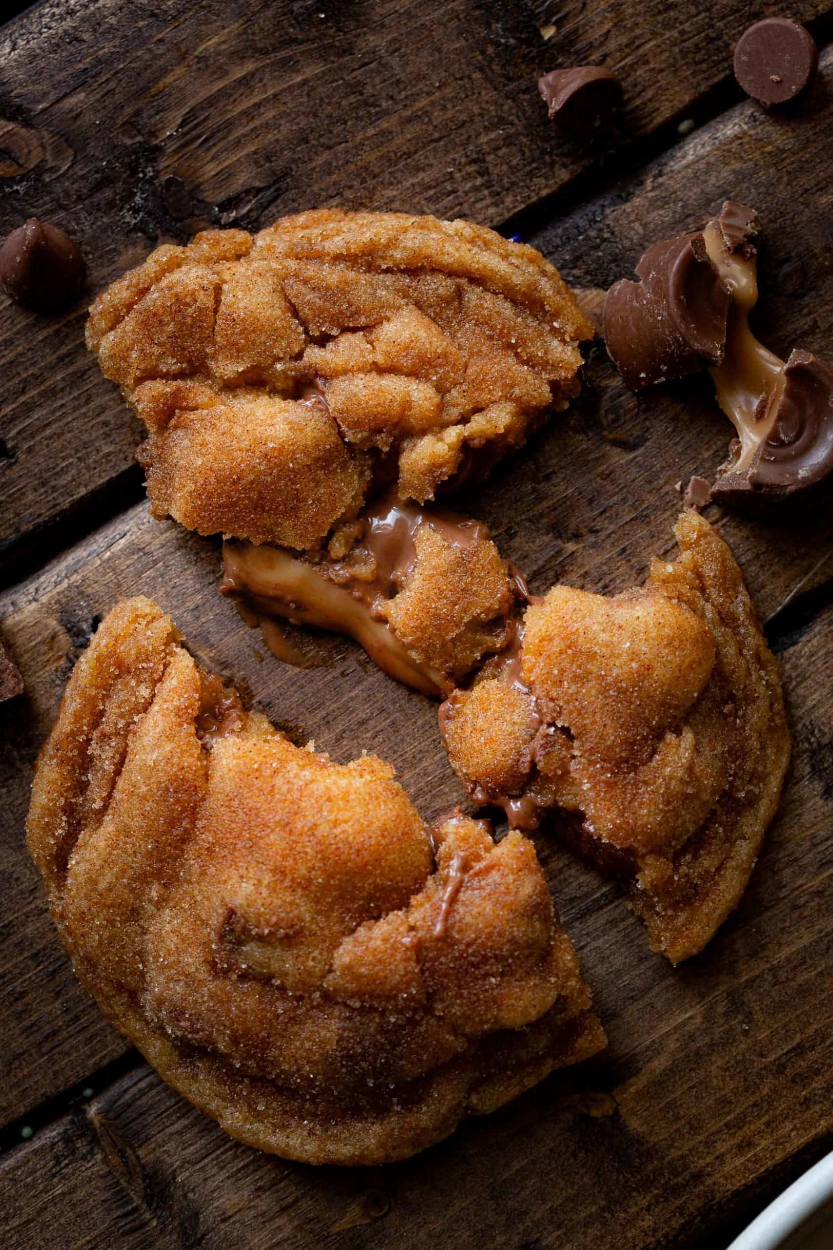 a photo taken above a Rolo stuffed pumpkin pudding cookie that has been broken into three pieces so you can see the gooey caramel center oozing out.