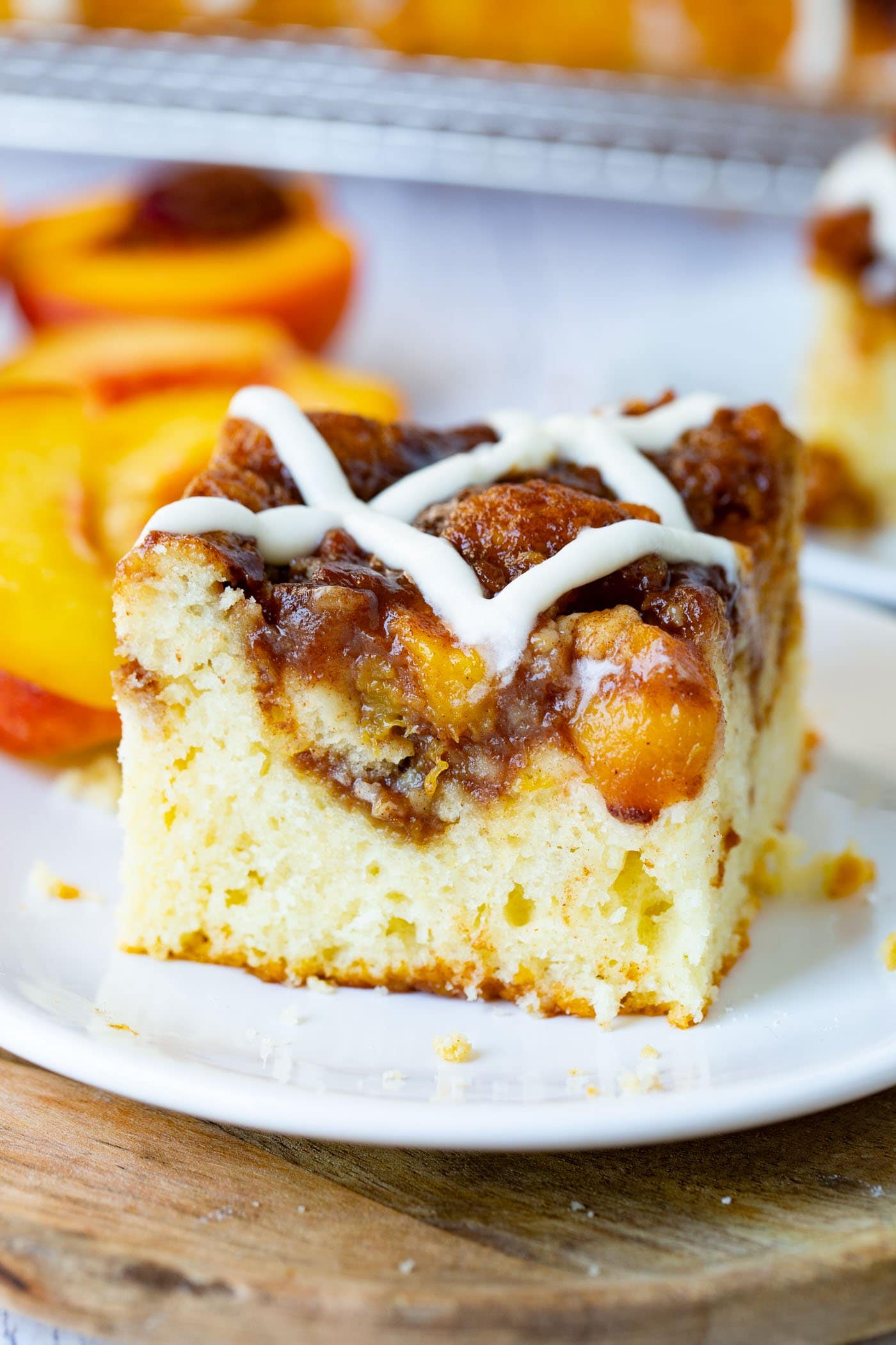 a photo of a single piece of peach coffee cake on a white plate with a sweet glaze on top of the cake