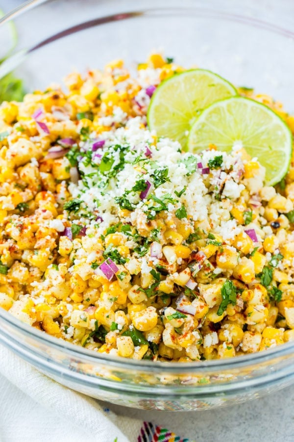 A glass bowl full of grilled corn, red onions, cilantro, crema, cotija cheese and lime juice which makes the best elote mexican grilled corn salad
