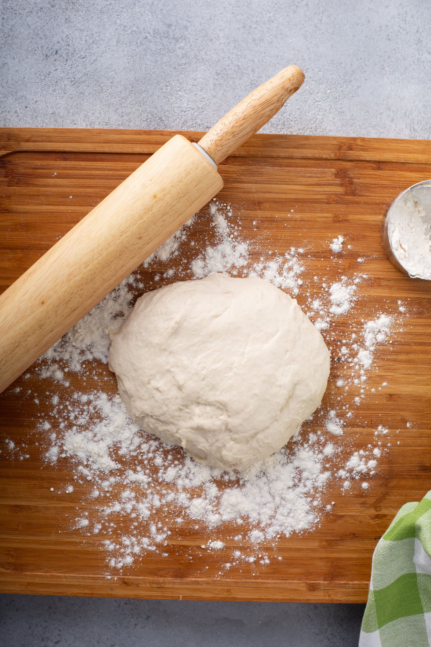 A photo of a mound of dough for unleavened bread sitting on a floured wooden cutting board with a wooden rolling pin sitting next to it.