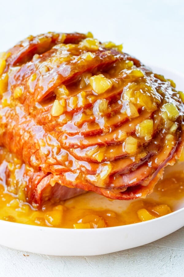 a photo of a spiral cut ham topped with a juicy pineapple glaze on a large white serving platter
