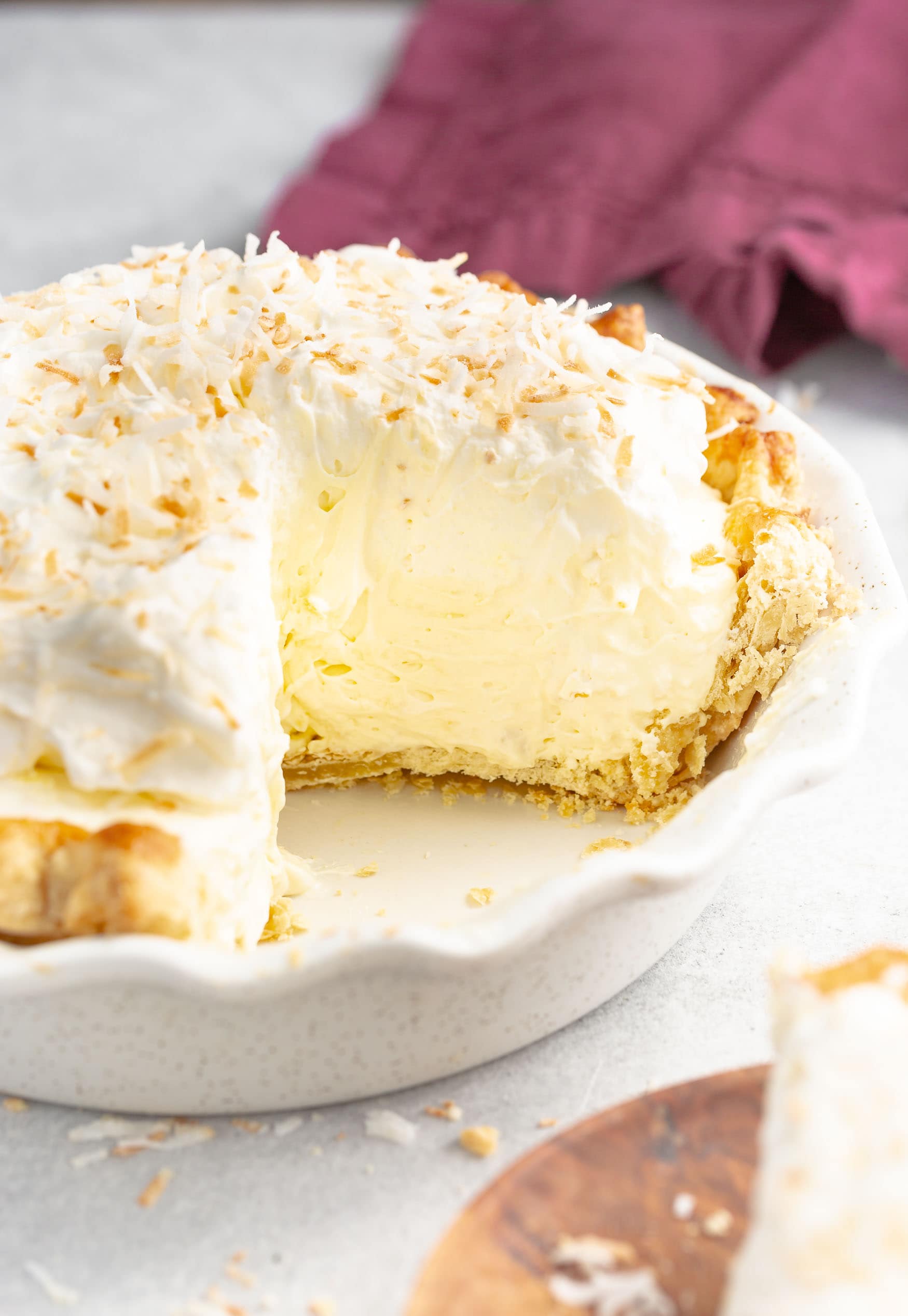 a photo of a thick and creamy coconut creamy pie with a couple of slices missing from the pie. the pie is topped with toasted coconut flakes.