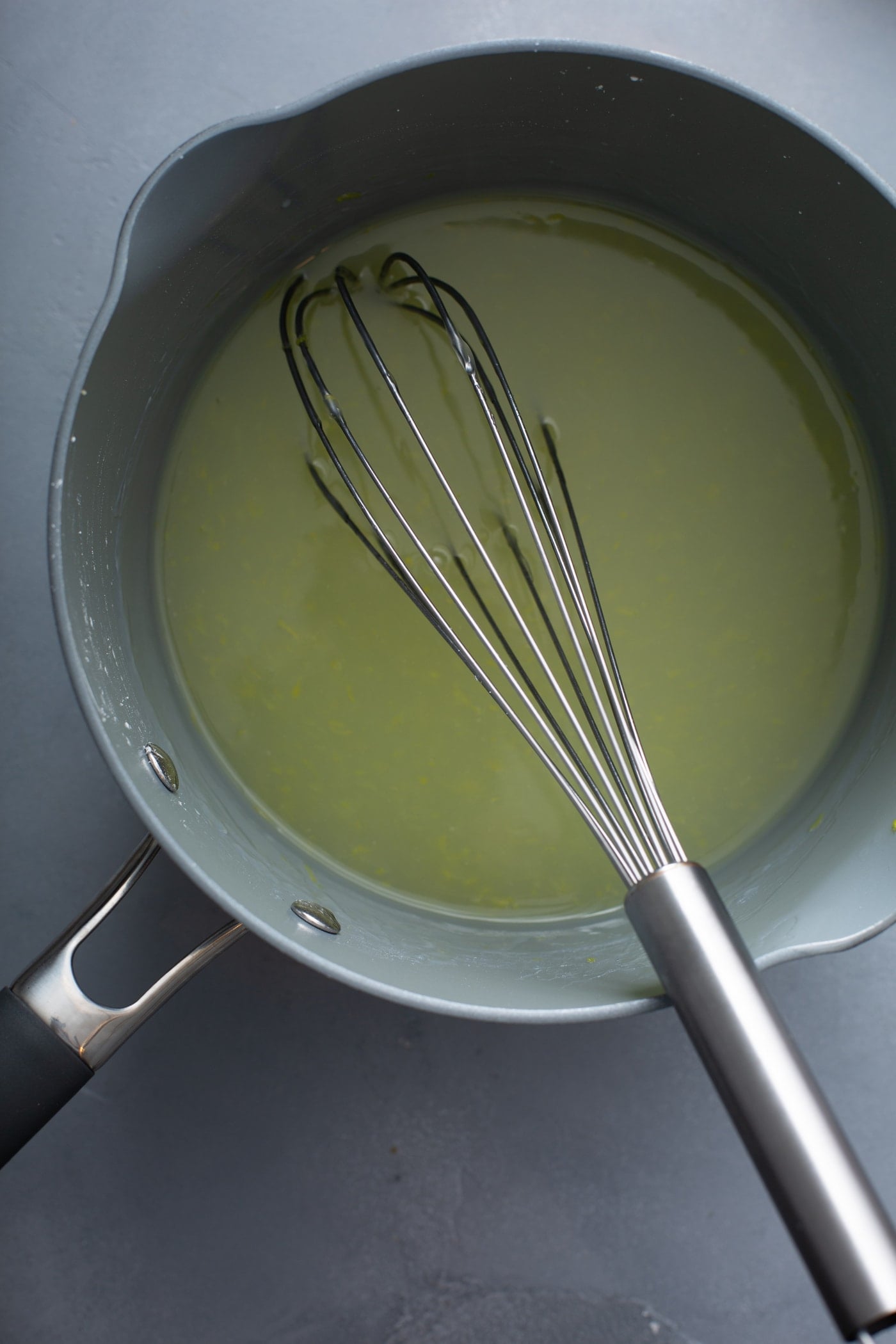 A sauce pan with lemon pie filling in it. It has a whisk resting in the filling.