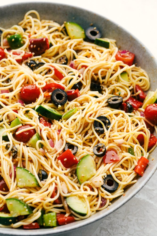 California spaghetti salad in a gray bowl with olives, tomatoes and fresh vegetables.  