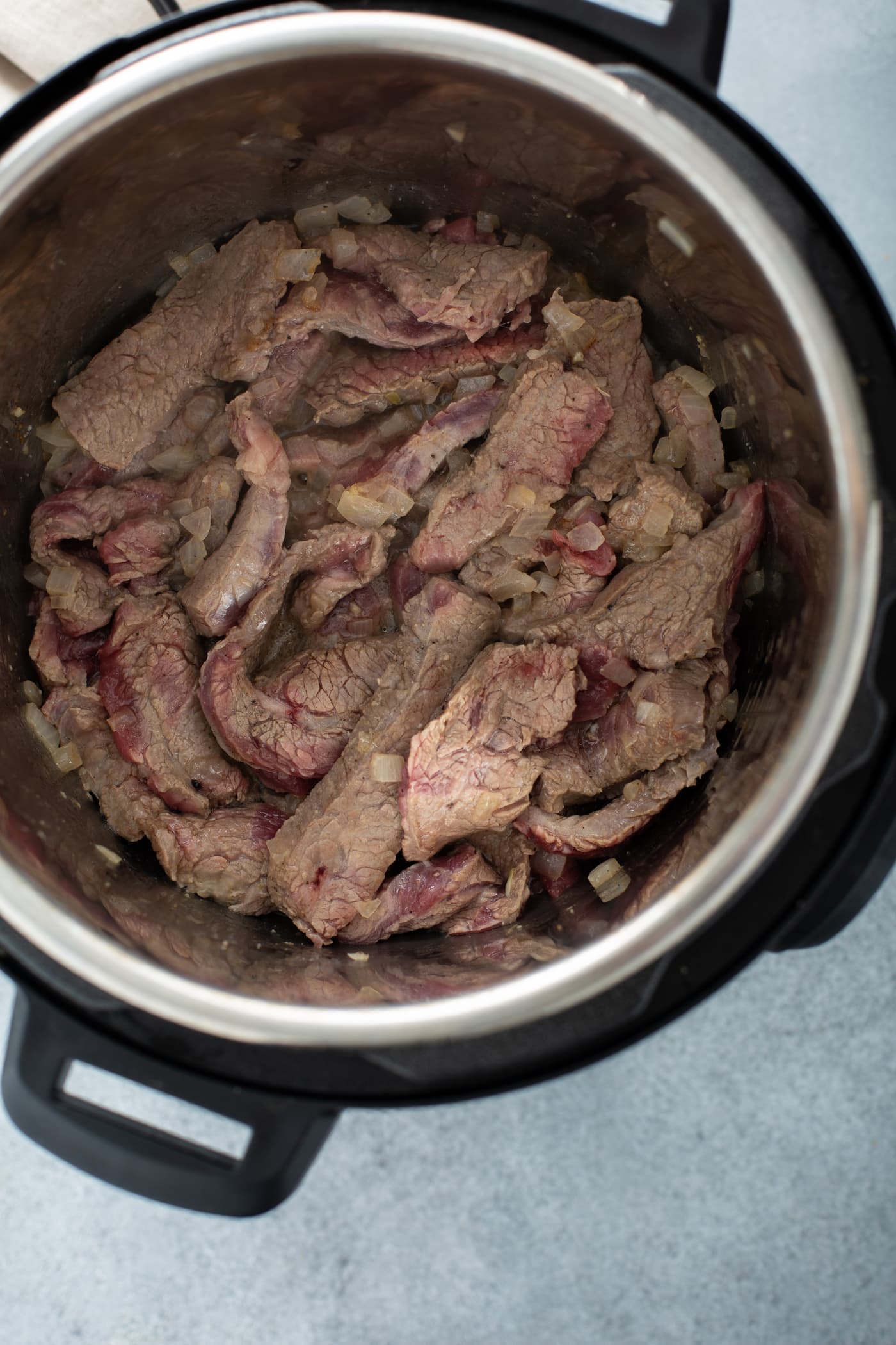A photo of sliced flank steak sauteeing in an Instant Pot.