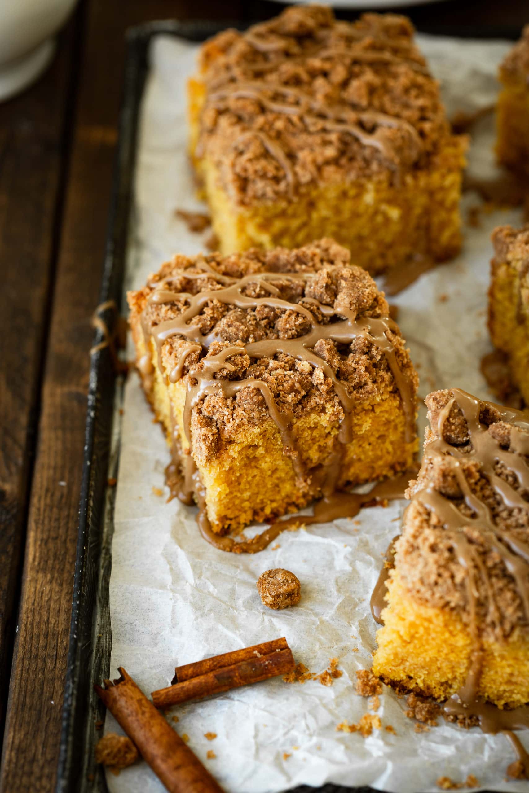 a photo of a baking sheet lined with parchment paper and topped with several pieces of fluffy pumpkin cake topped with cinnamon streusel and maple glaze.